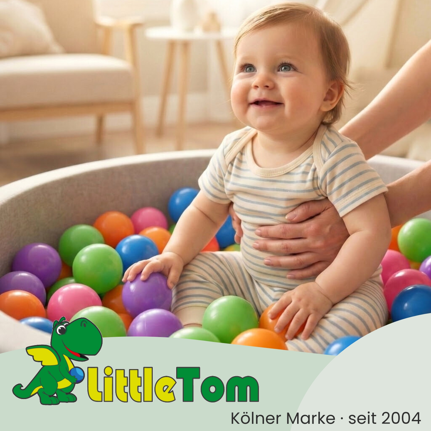 Ein Baby sitzt in einem Bällebad mit bunten Bällen und einem Logo.
