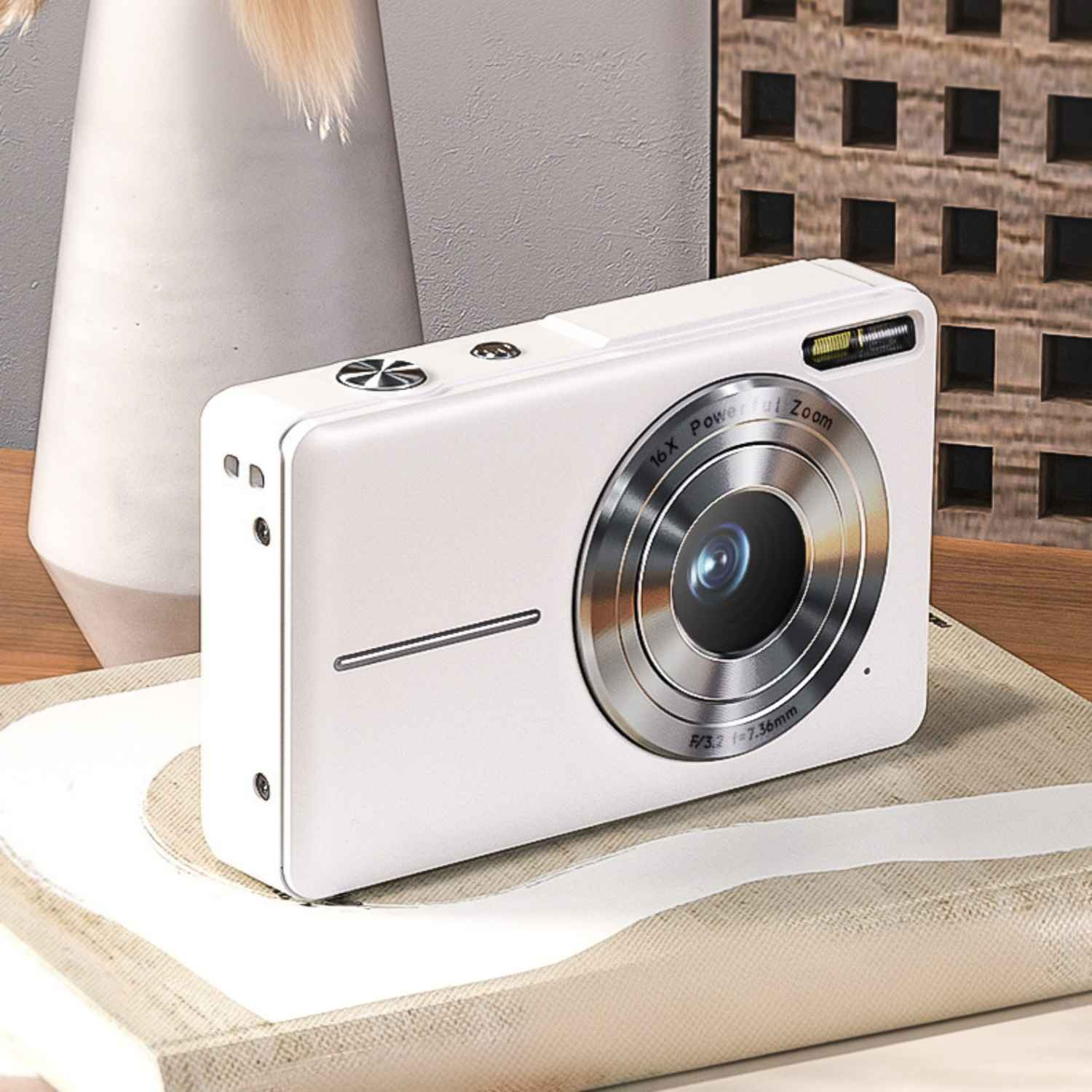 Eine weiße Digitalkamera mit 16-fachem Zoom liegt auf einem hellen Stoff.