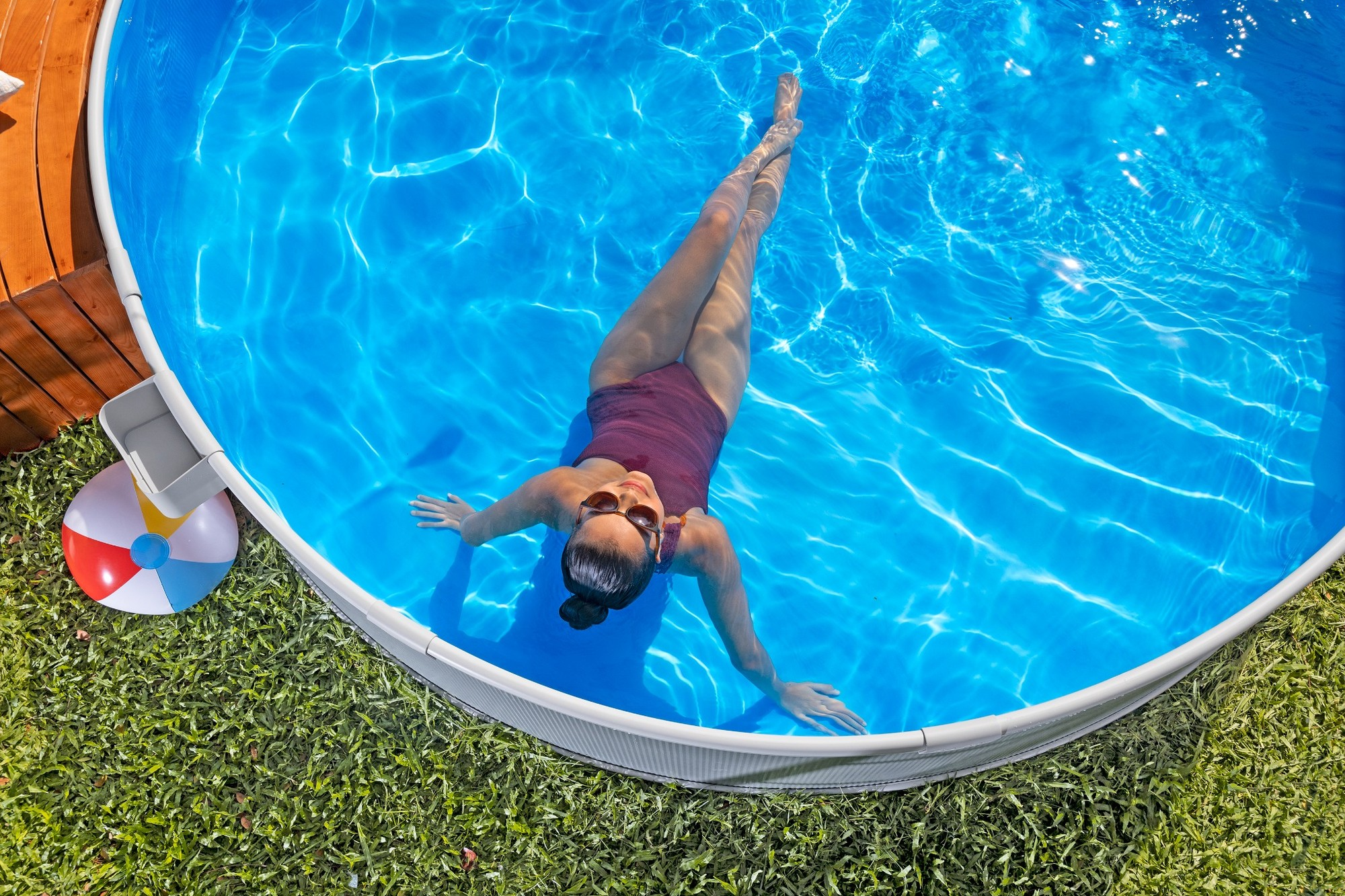 Frau entspannt im Pool, Ball und Holzdeck im Gras.
