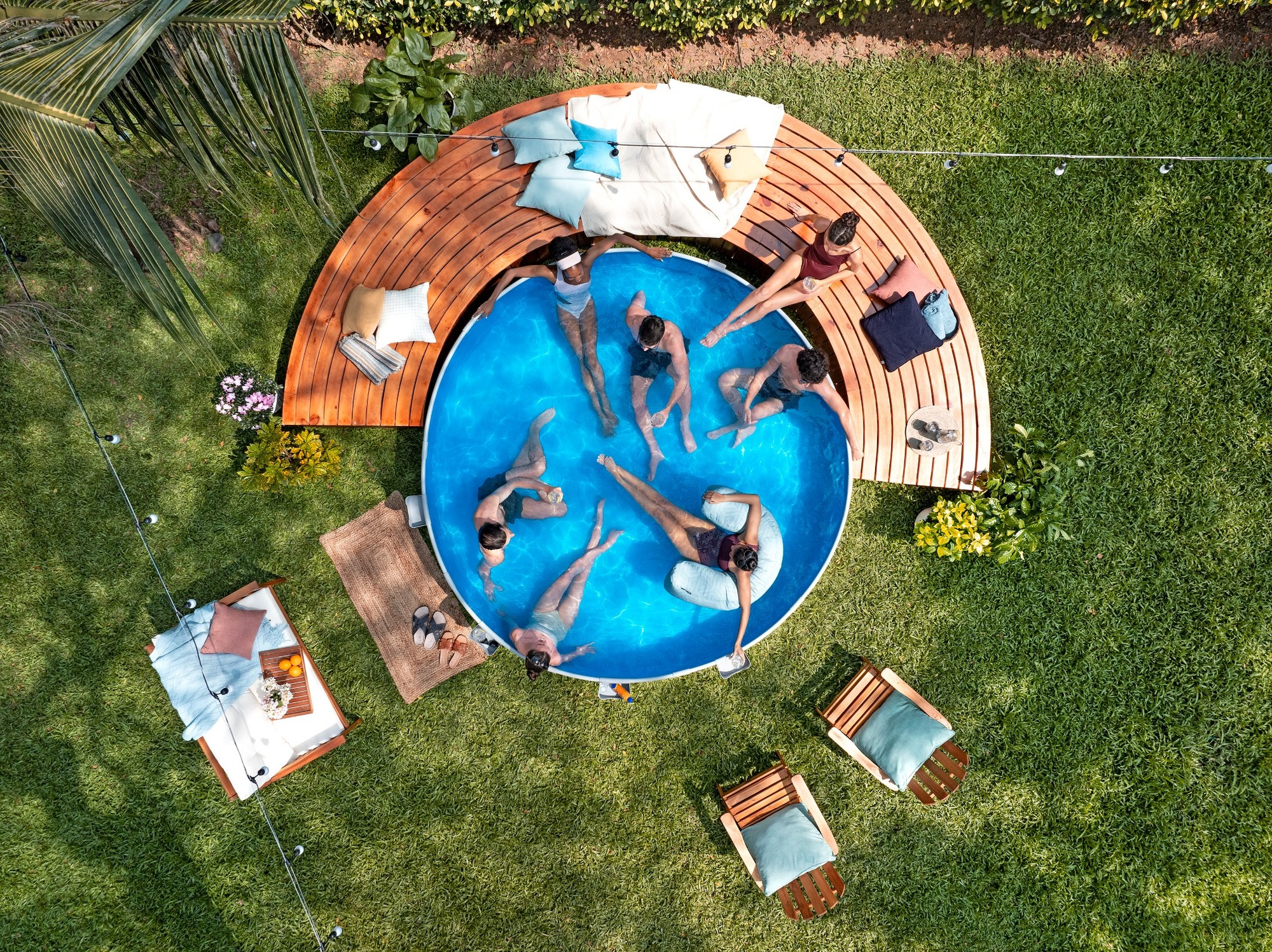 Menschen entspannen sich in einem Pool und auf einer Holzterrasse in einem Garten.