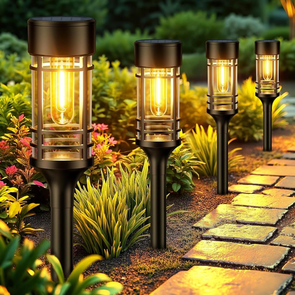 Vier Solar-Gartenleuchten beleuchten einen Steinweg im Abendlicht.