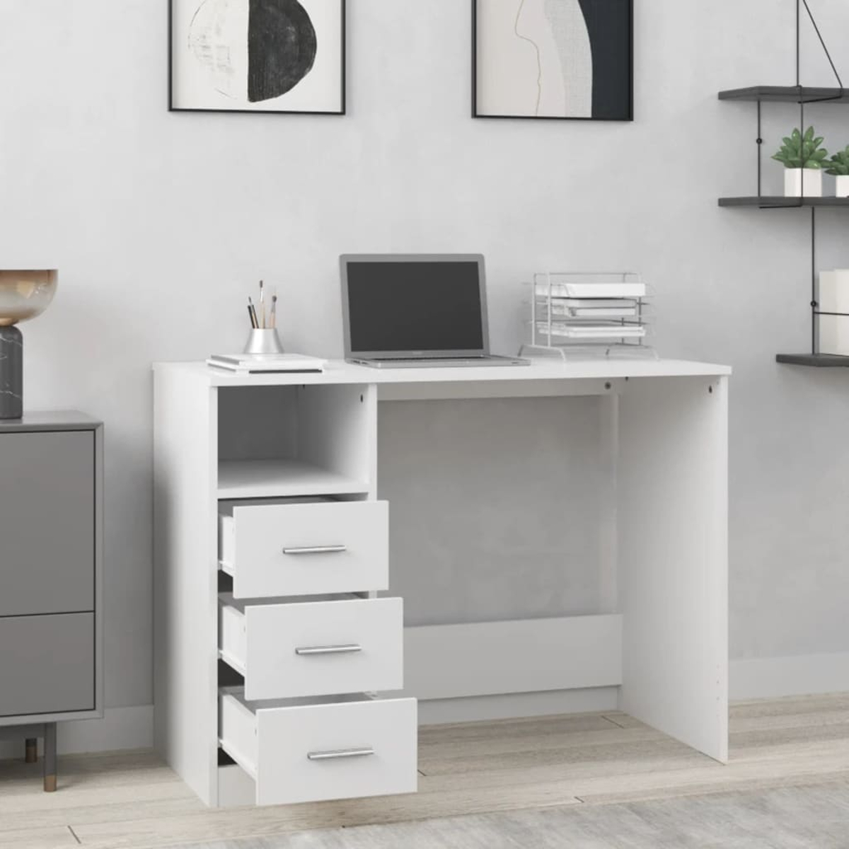 Ein weißer Schreibtisch mit Laptop, Schubladen und Büromaterial. Dekorative Bilder an der Wand.