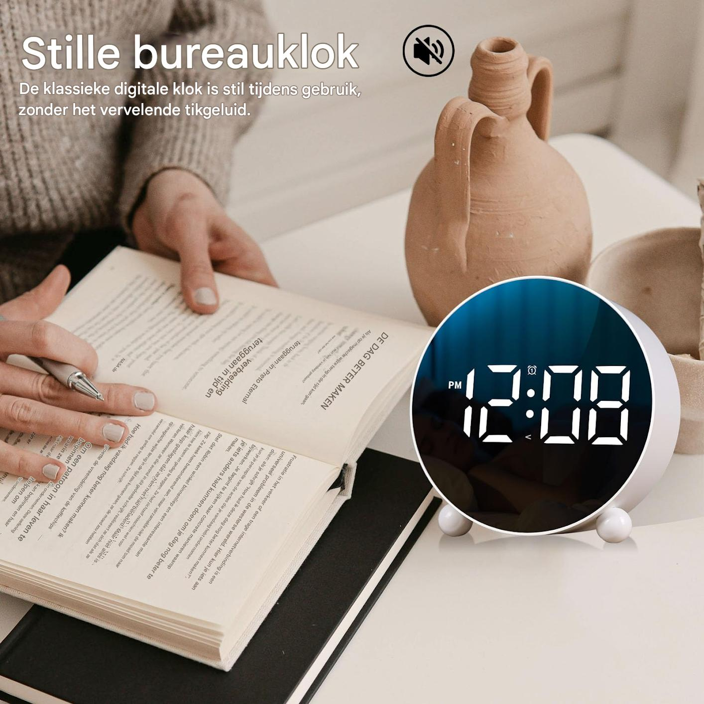 Ein weißer digitaler Wecker zeigt 12:08 Uhr an, neben einem Buch und Keramik.
