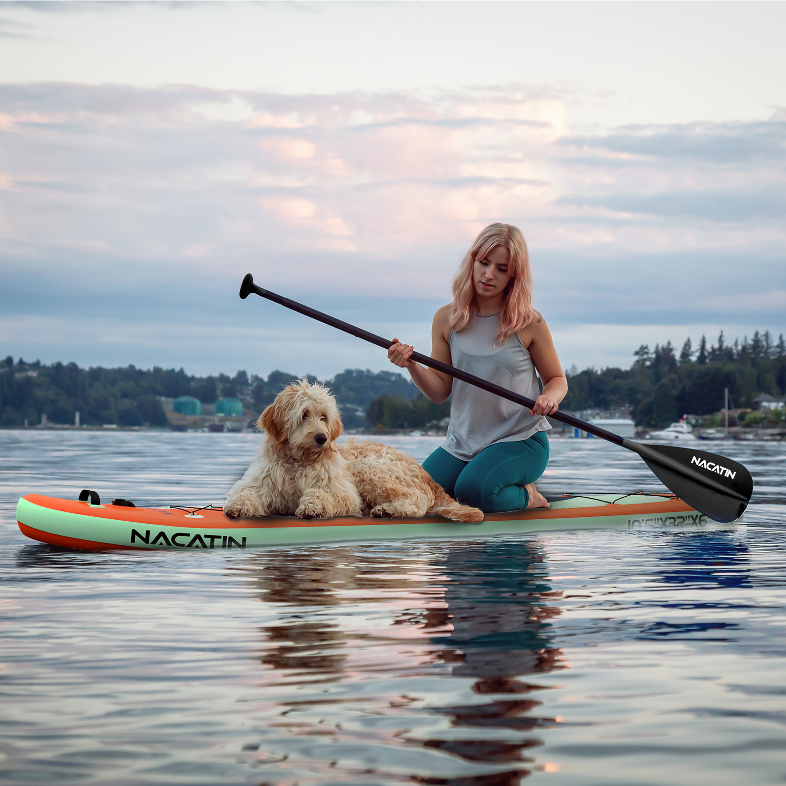 Frau und Hund auf Paddleboard auf Wasser in der Dämmerung mit Bäumen im Hintergrund.