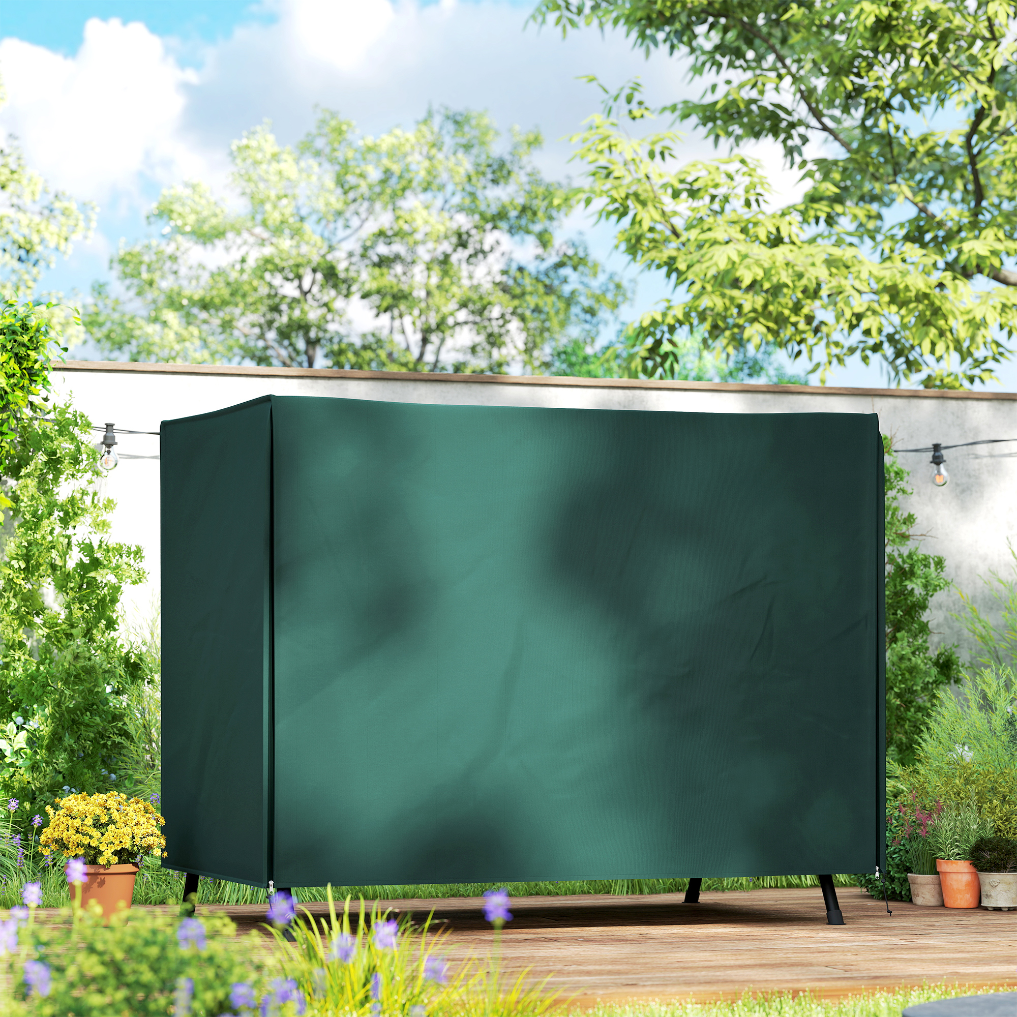 Funda verde oscura para muebles de exterior en tarima de madera, con plantas y cielo azul.