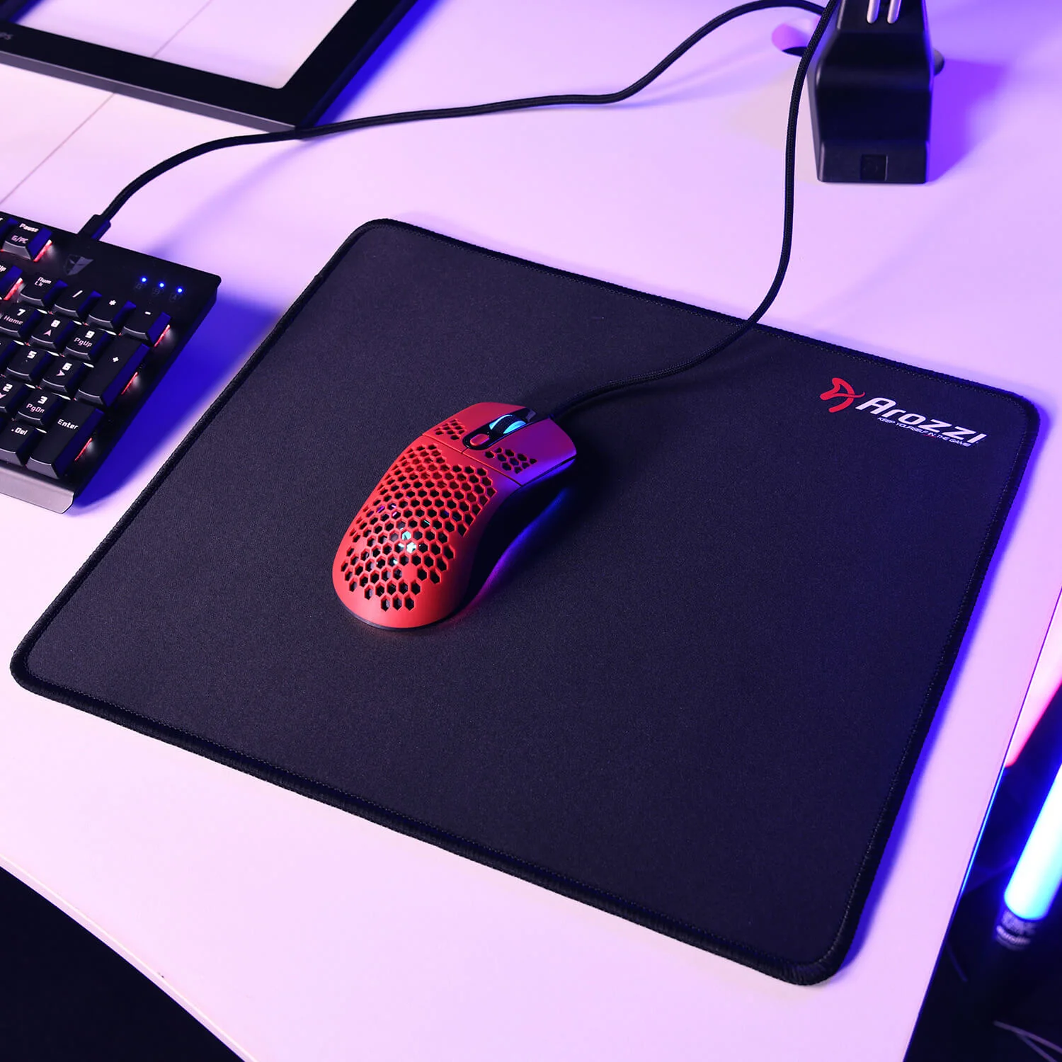 Un mouse da gaming rosso riposa su un tappetino Arozzi nero accanto a una tastiera.