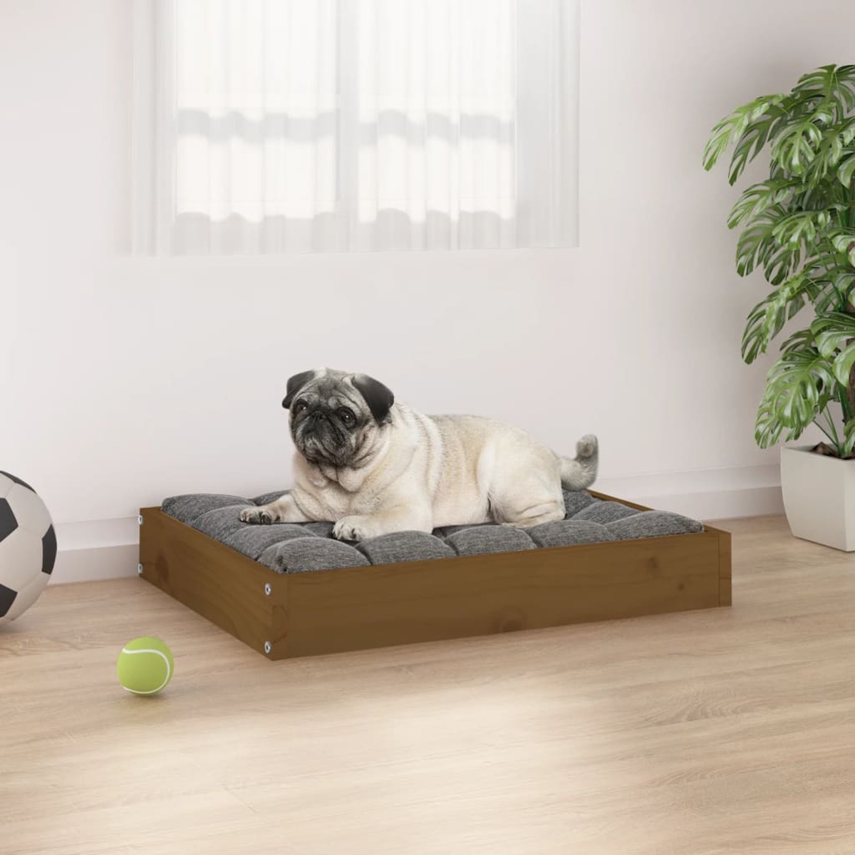 Ein Mops ruht auf einem Hundebett aus Holz mit grauem Kissen. Ein Tennisball und Fußball sind in der Nähe.