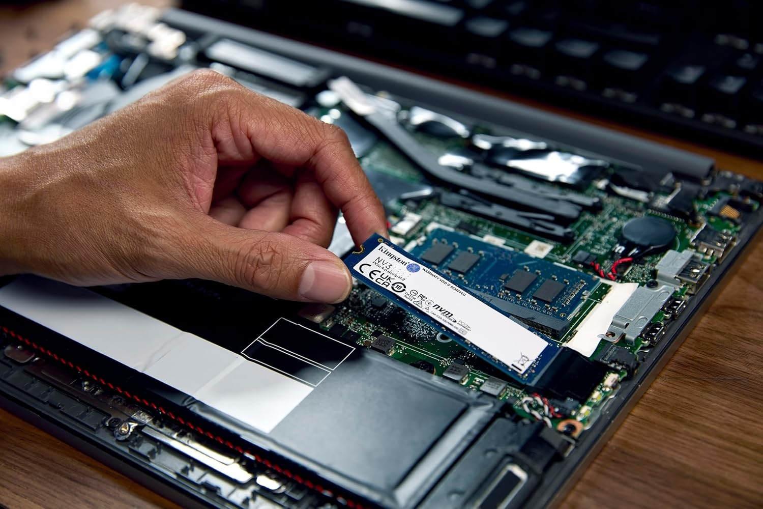 Eine Hand hält eine M.2 SSD über die Platine eines geöffneten Laptops.