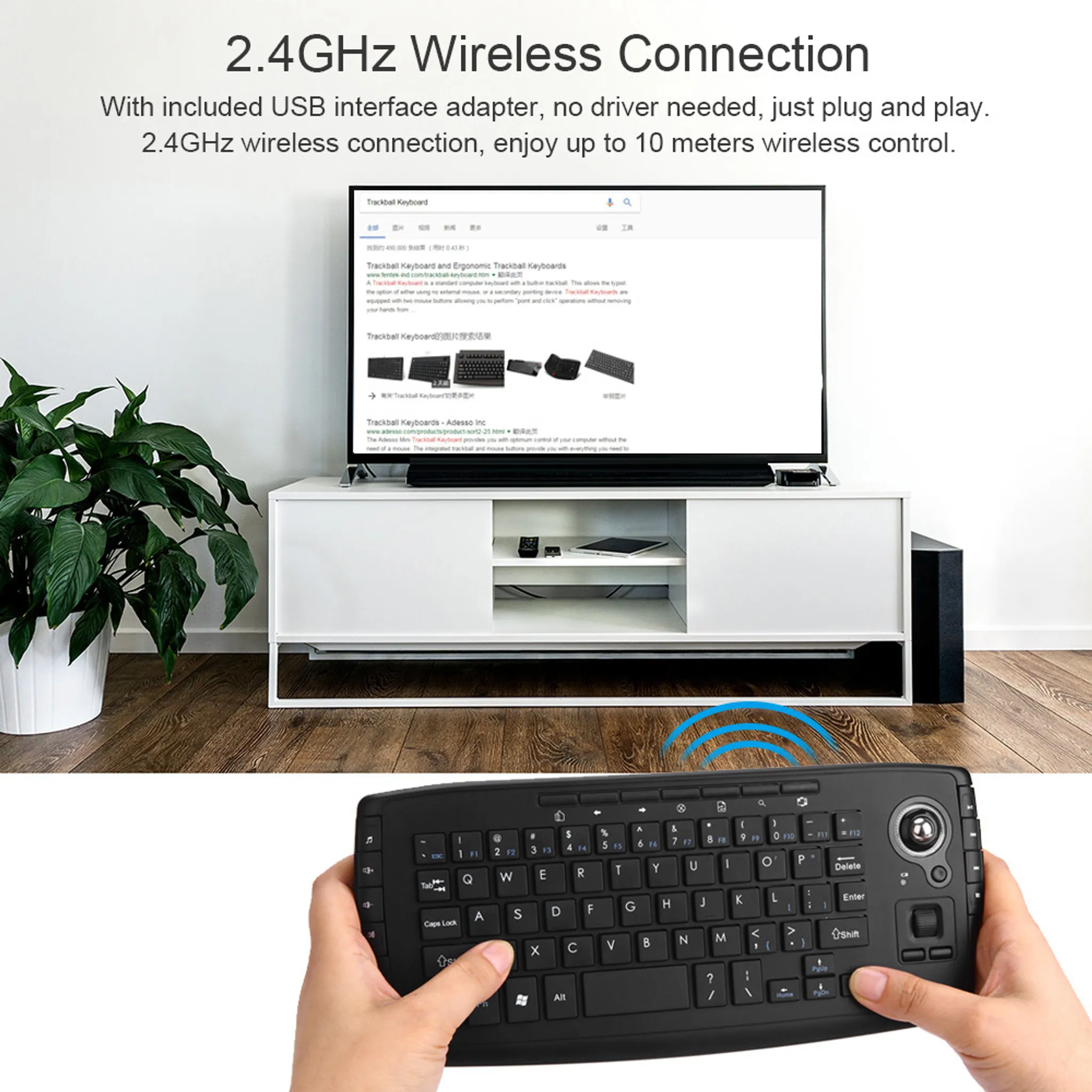 Eine Hand hält eine schwarze Tastatur mit Trackball. Ein Fernseher steht auf einem weißen Schrank.