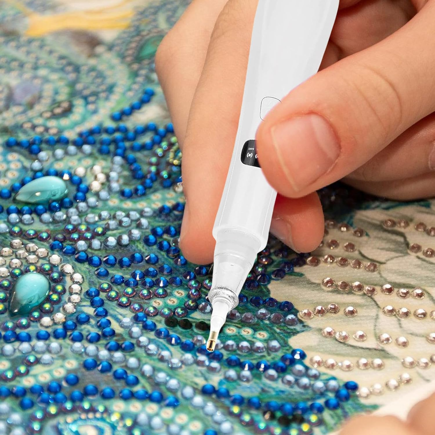 Hand benutzt Diamant-Malstift, um blaue und silberne Perlen auf Leinwand zu setzen.