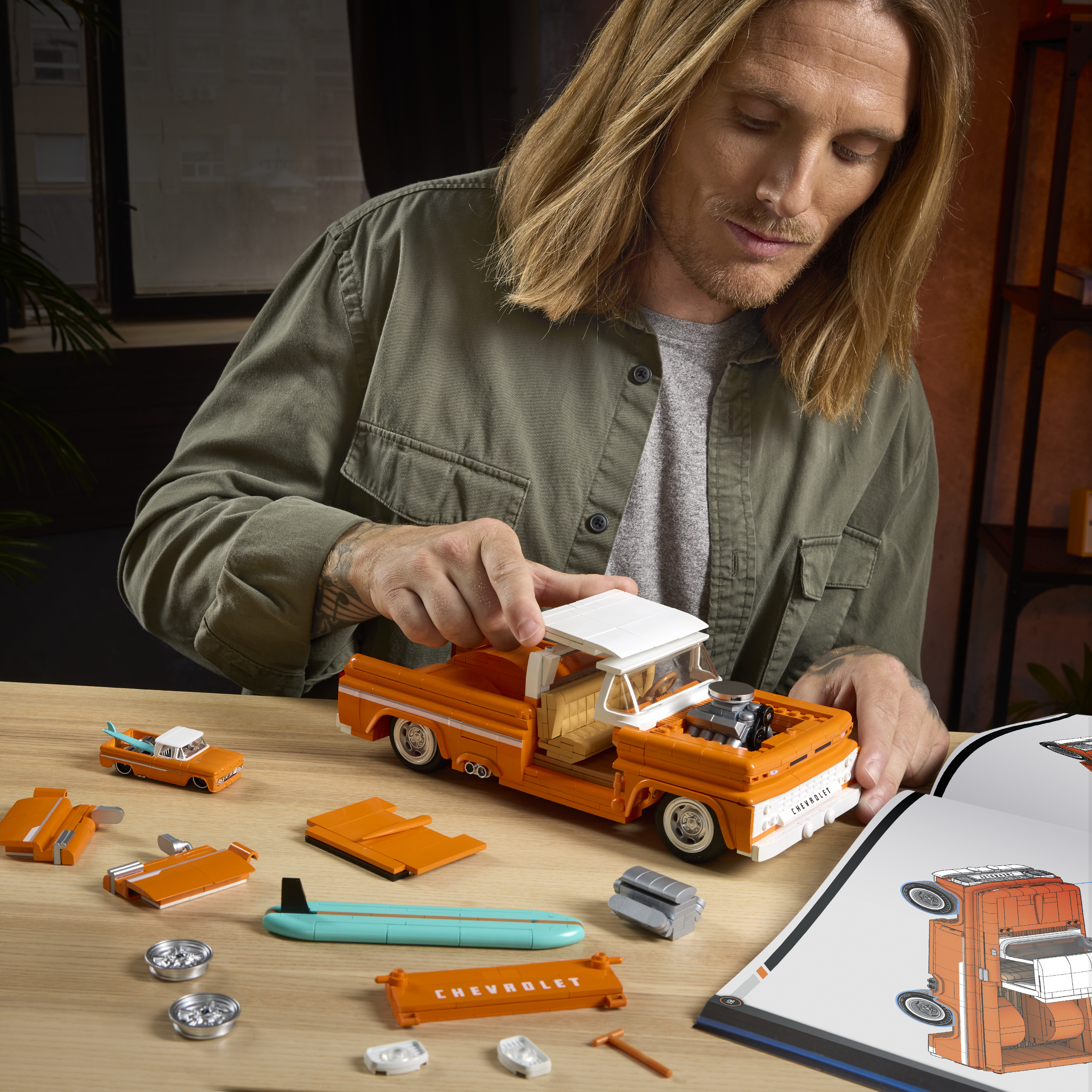 Uomo che costruisce un camion Lego arancione con tetto bianco e tavola da surf.