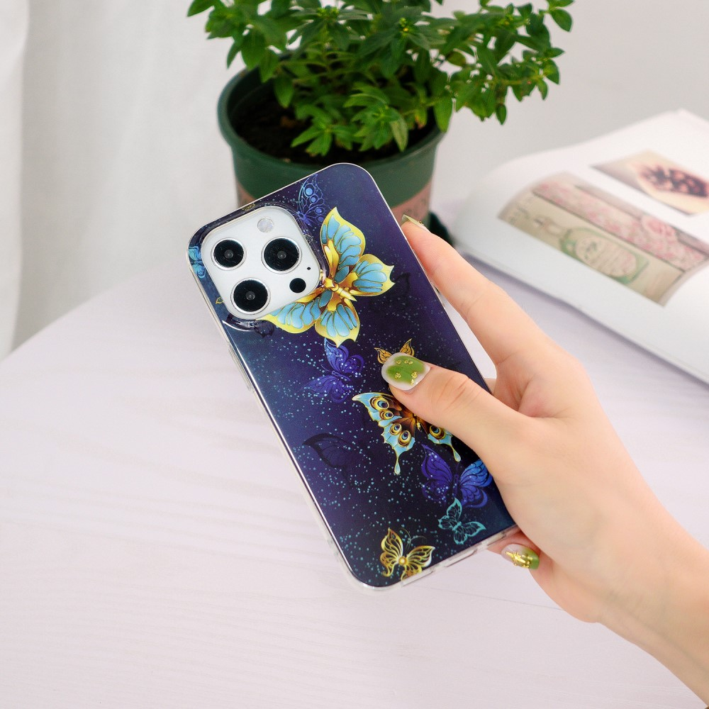 Una mano tiene una cover per telefono blu scuro con disegni di farfalle. Uno sfondo con pianta e libro.