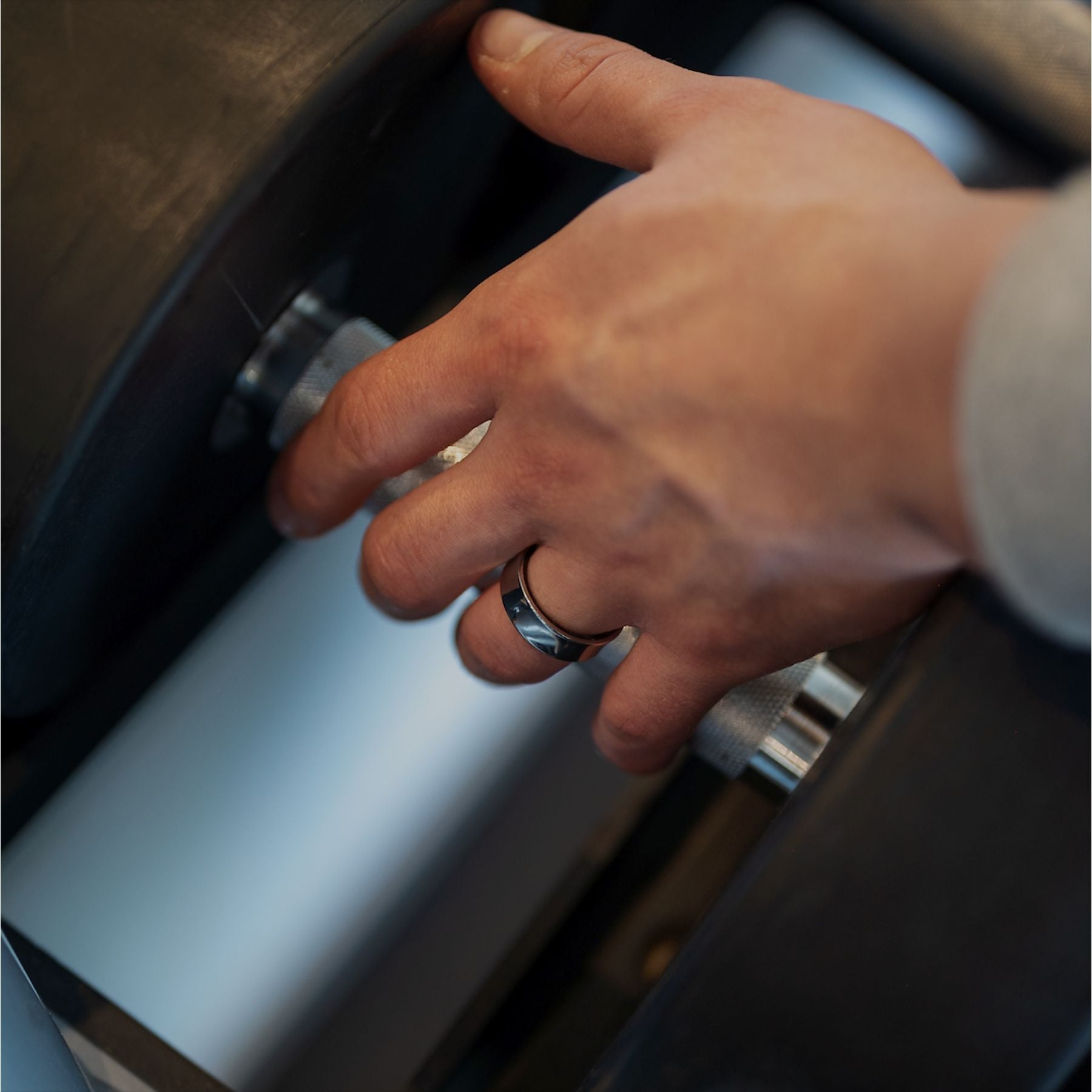Eine Hand mit Ring stellt ein Gewicht an einer Hantel ein.