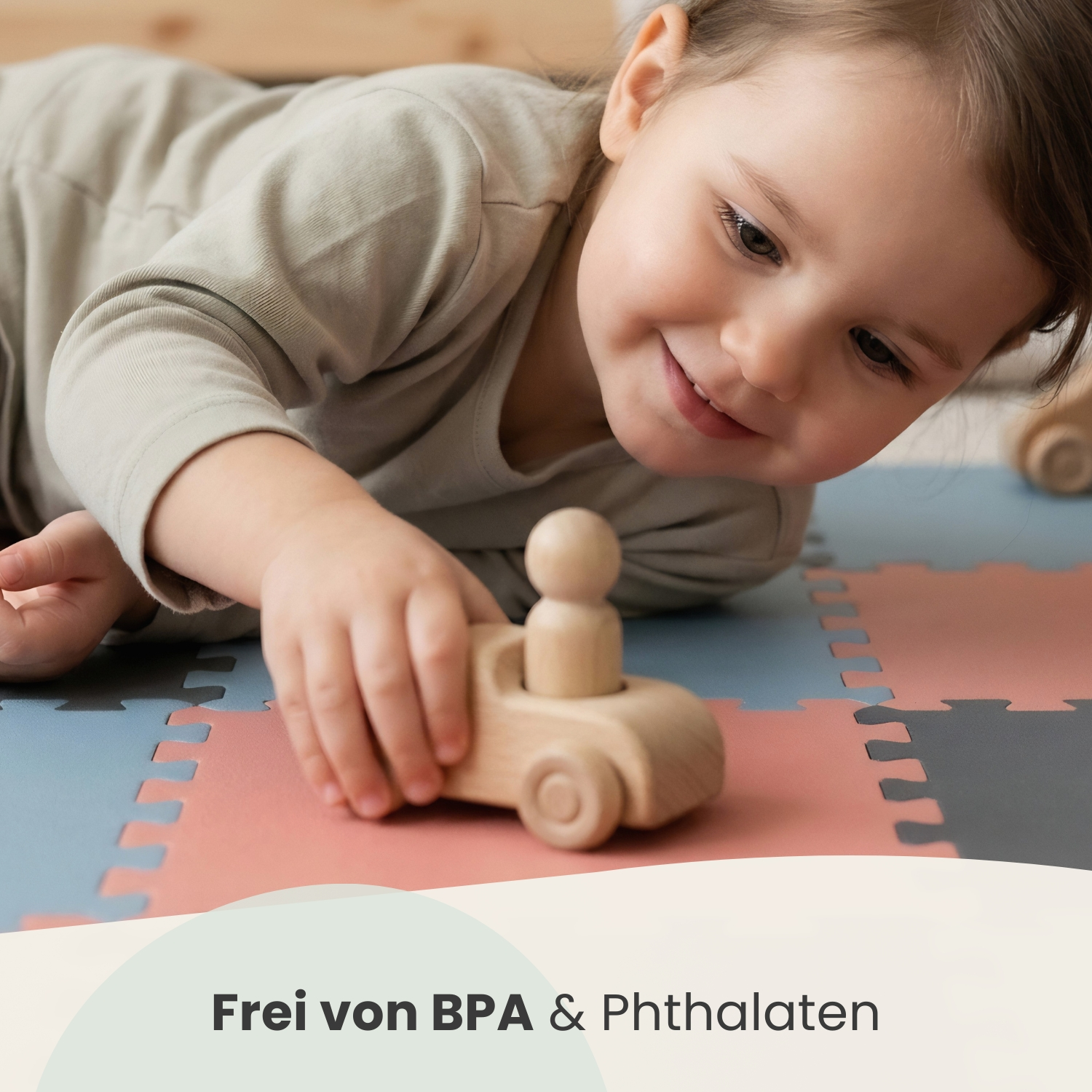 Ein kleines Mädchen liegt auf dem Boden und spielt mit einem Holzauto.