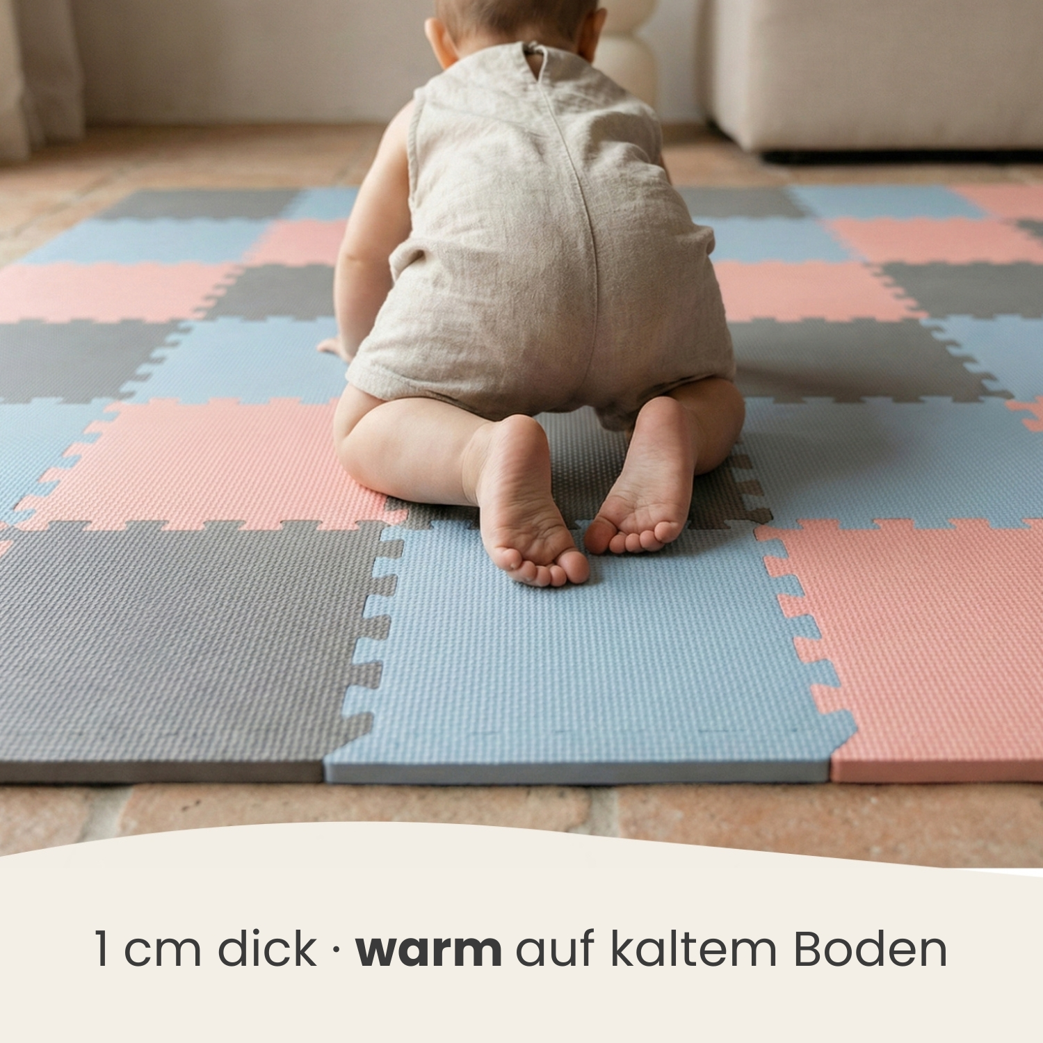 Baby krabbelt auf einer bunten Puzzlematte aus rosa, blauen und grauen Teilen.
