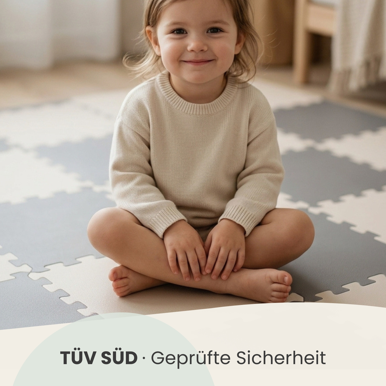 Ein lächelndes Kleinkind sitzt im Schneidersitz auf einer grauen und weißen Puzzlematte.