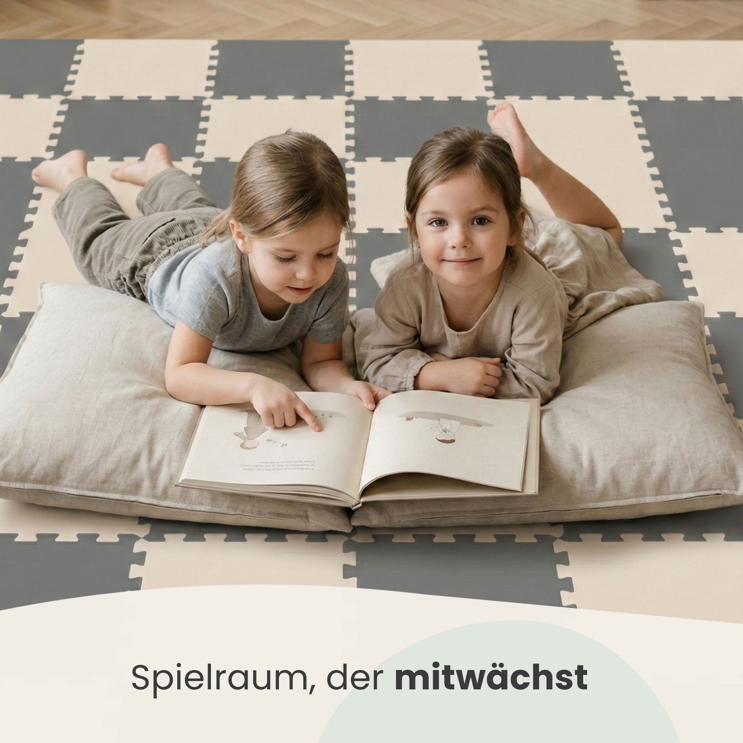 Zwei Mädchen liegen auf einem Kissen und lesen ein Buch auf einer gemusterten Matte.