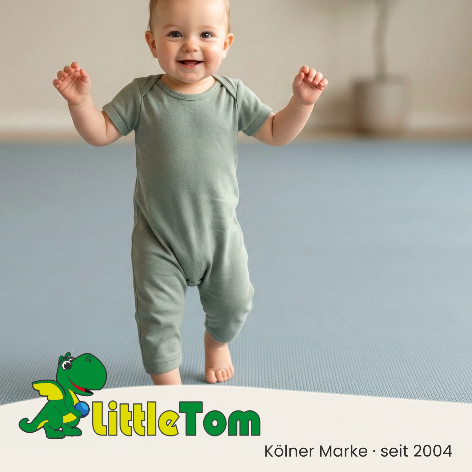 Ein lächelndes Baby in einem hellgrünen Strampler steht auf einem blauen Boden.