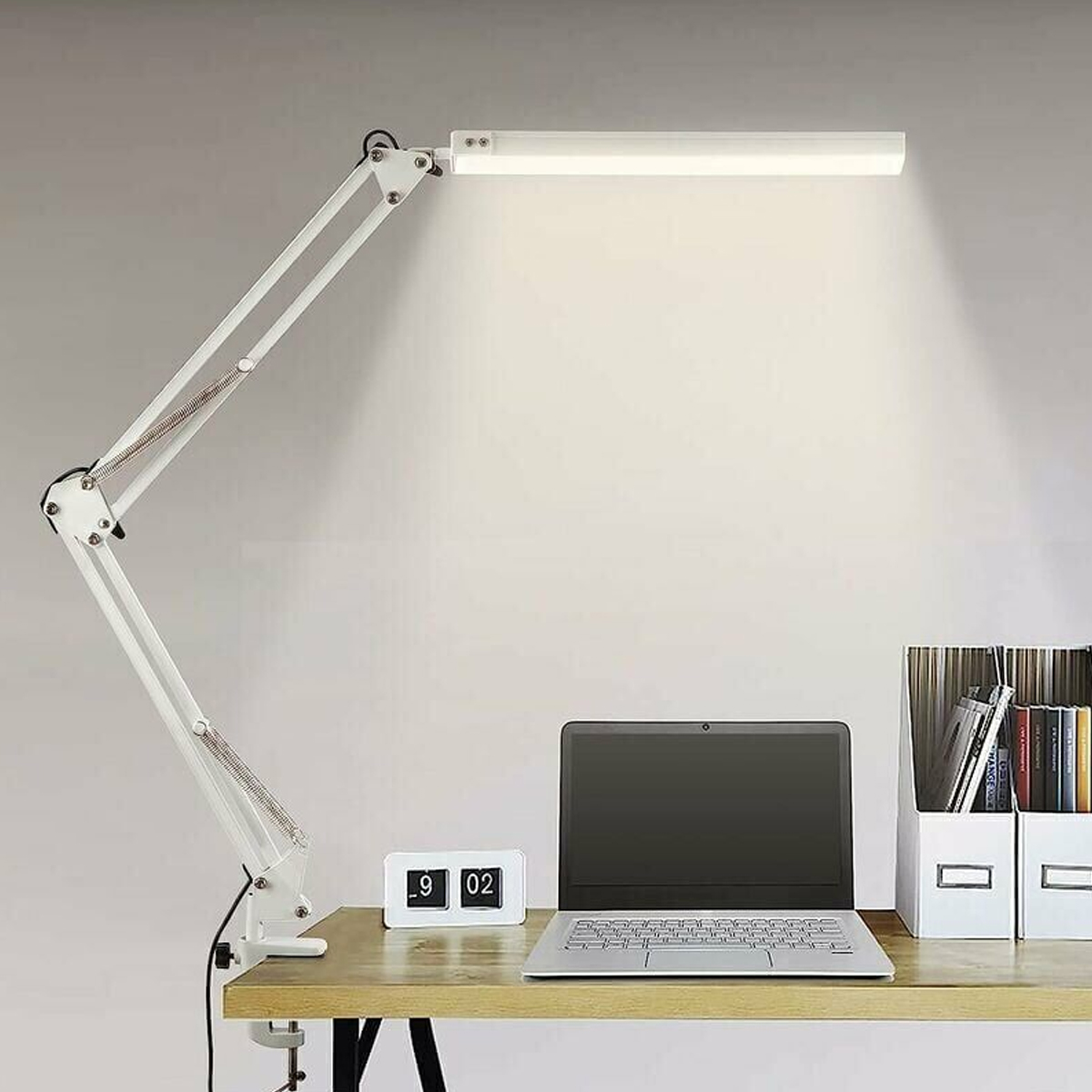Ein weißer Schreibtisch mit Laptop, Uhr und Lampe.