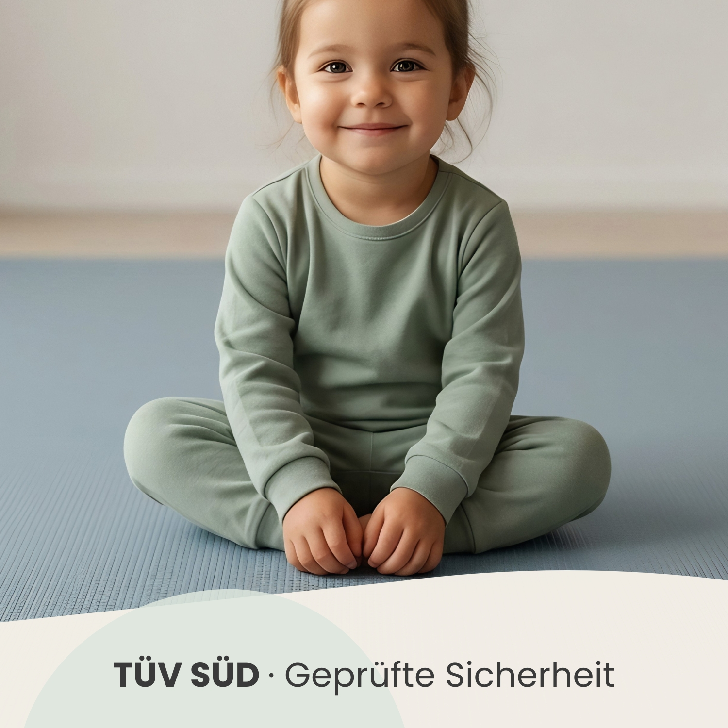Ein kleines Mädchen in einem grünen Outfit sitzt lächelnd auf einer blauen Matte.