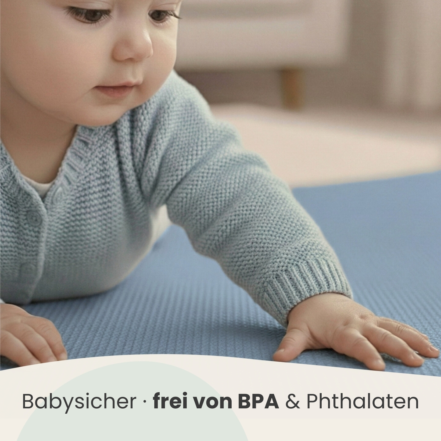 Baby in blauem Strickcardigan liegt auf blauer Matte, handgestützt.