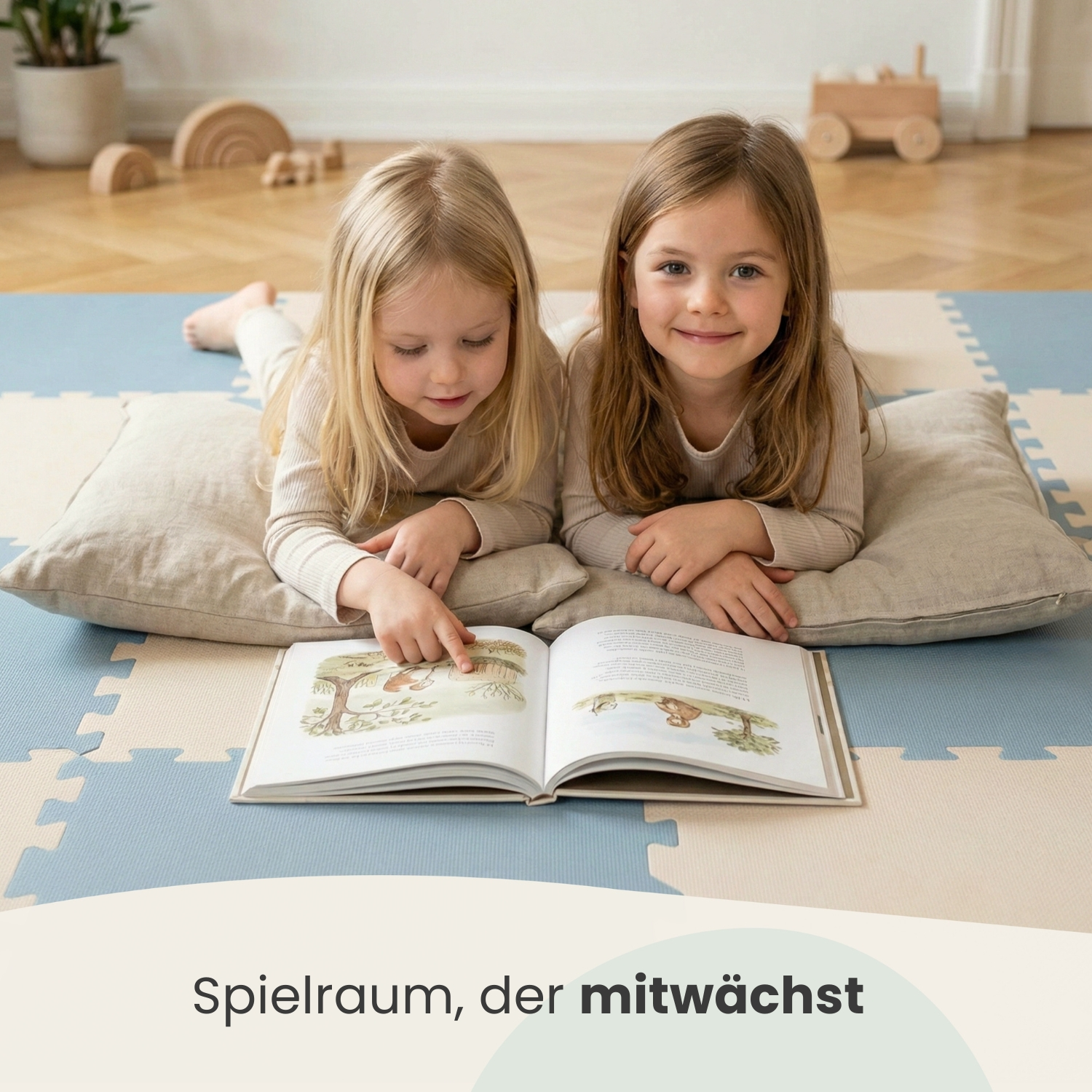 Zwei Mädchen liegen auf dem Boden und lesen ein Buch. Im Hintergrund Holzspielzeug.