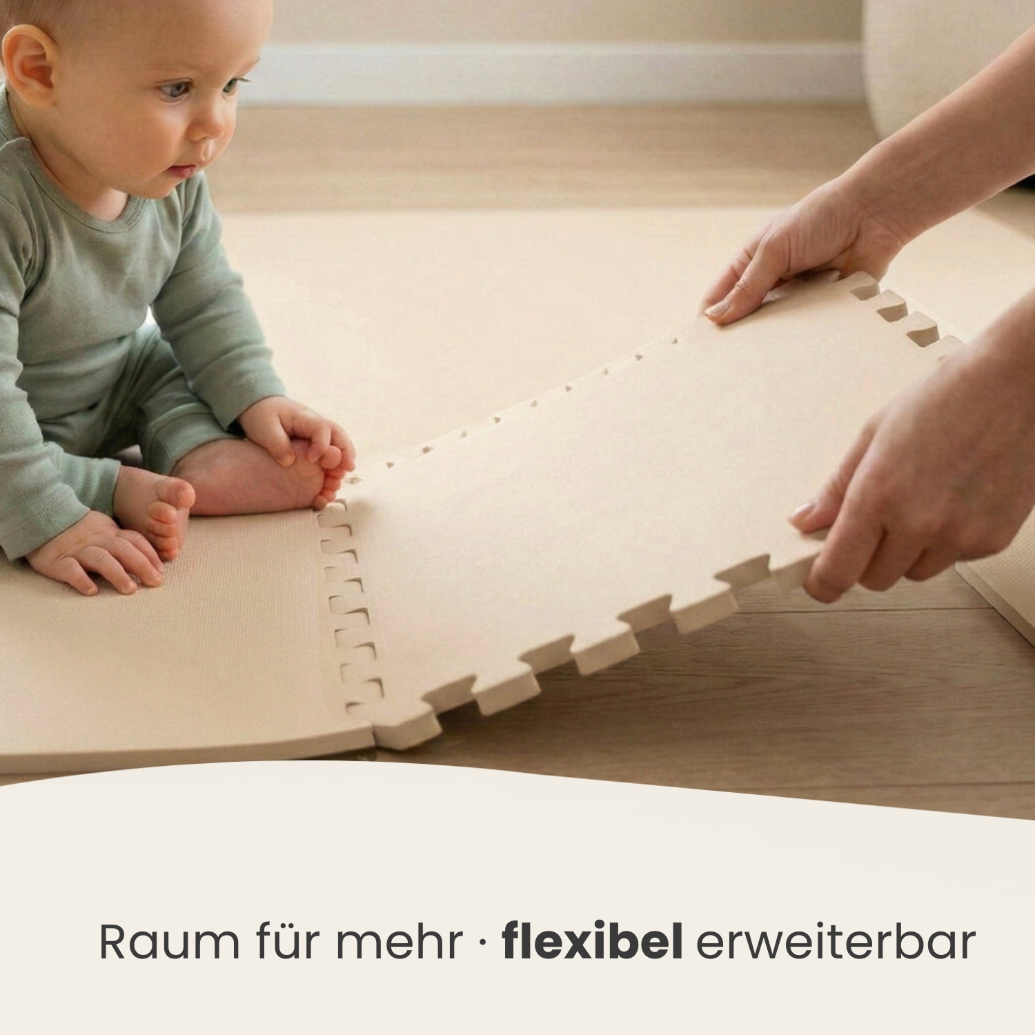 Ein Baby in einem grauen Strampler sitzt neben einer Person, die eine Puzzlematte legt.