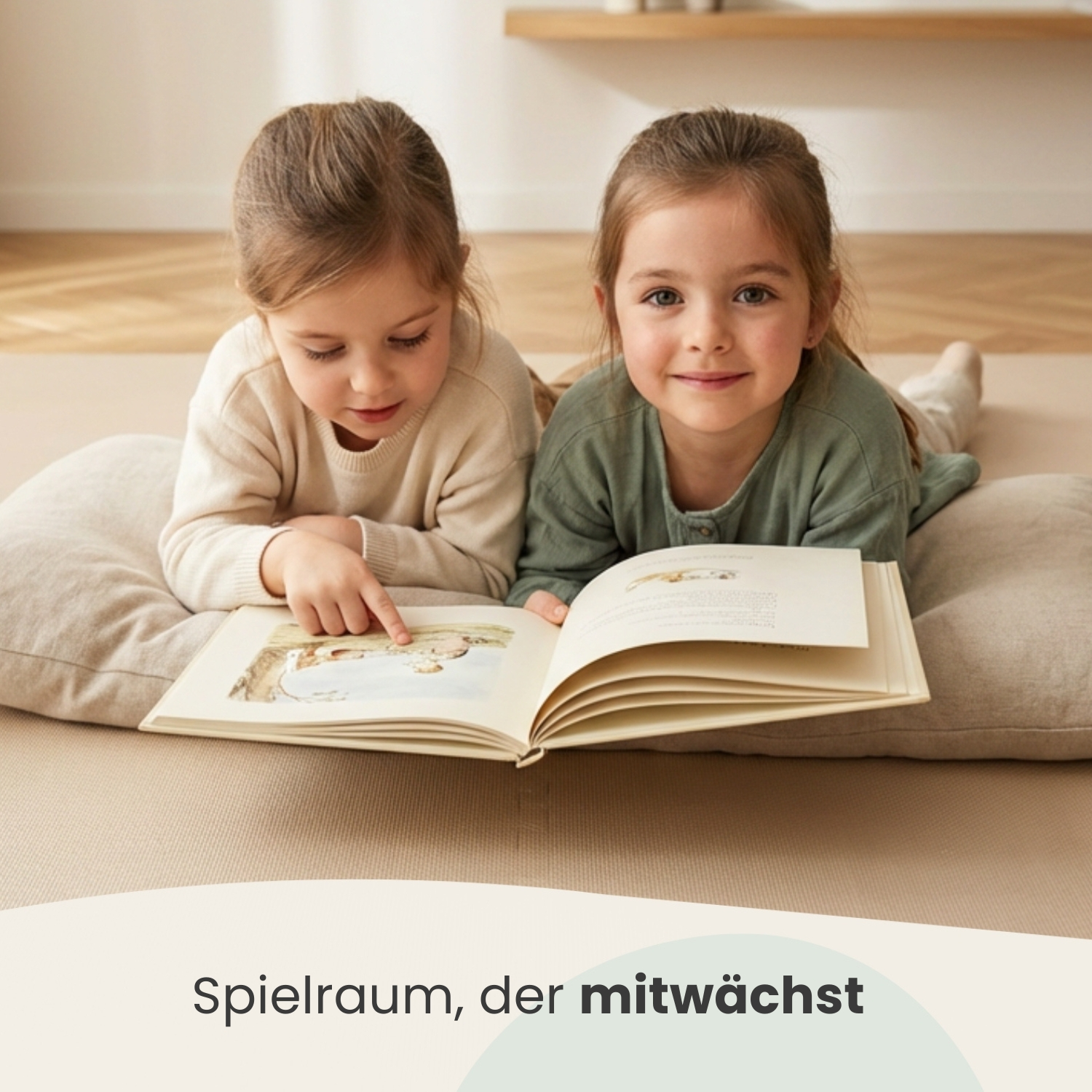 Zwei Mädchen liegen auf einem Kissen und lesen ein Buch. Ein Mädchen zeigt auf eine Seite.