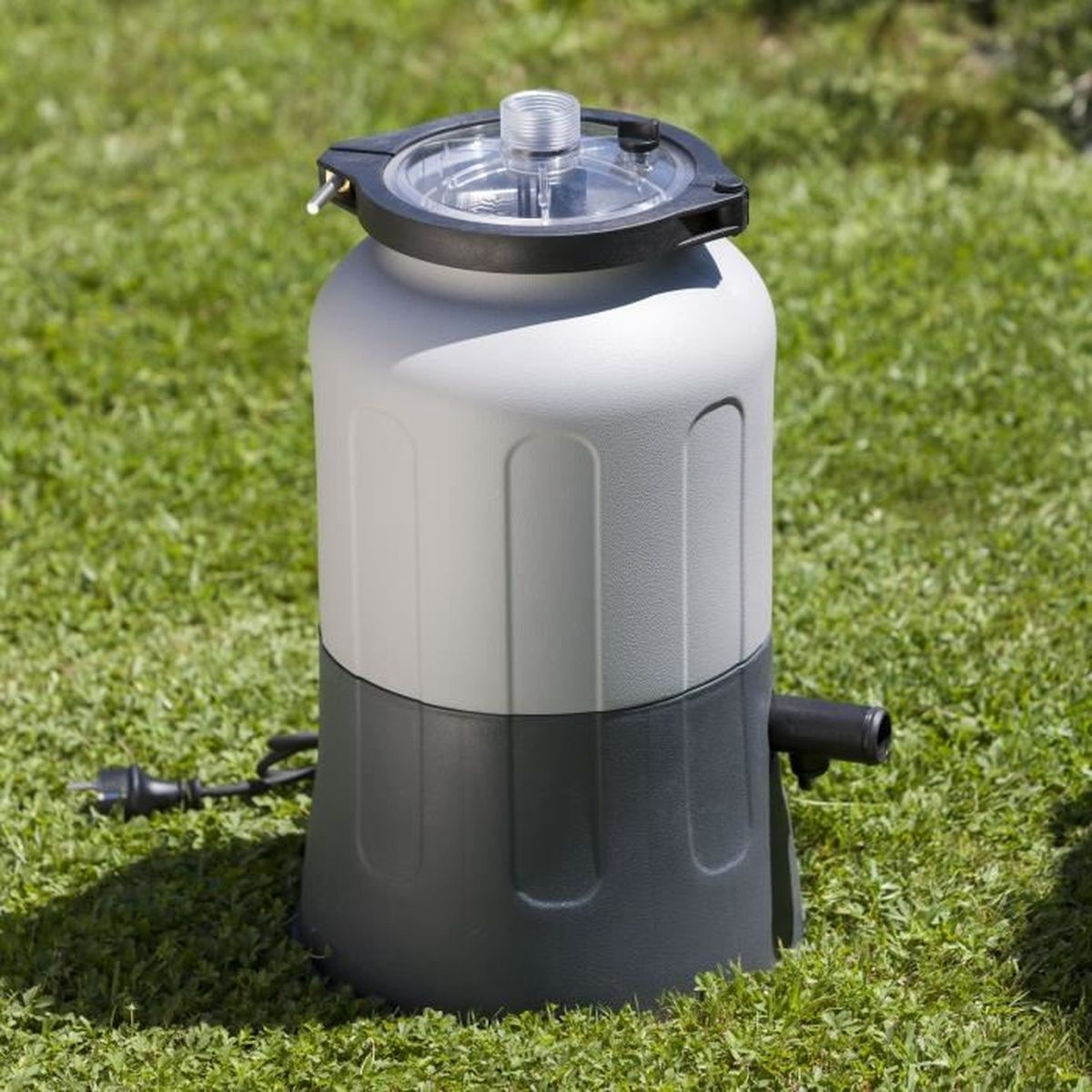 Ein grauer und weißer Poolfilter steht auf grünem Gras mit einem Kabel.