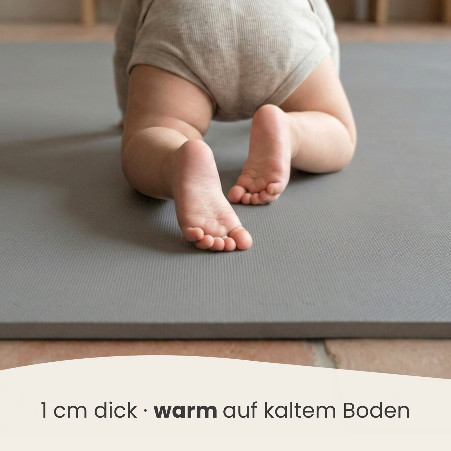 Baby krabbelt auf grauer Matte. Füße im Vordergrund. Text unten.