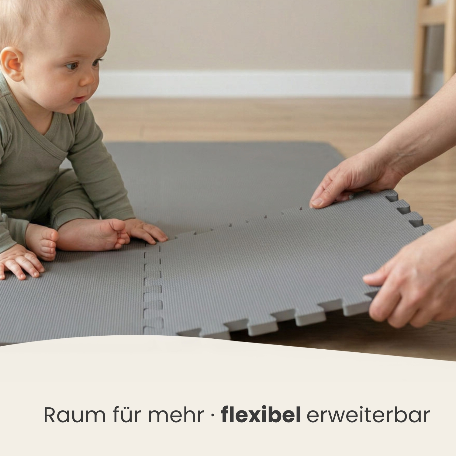 Ein Baby in einem grauen Strampler sitzt auf einer grauen Matte, die eine Hand erweitert.