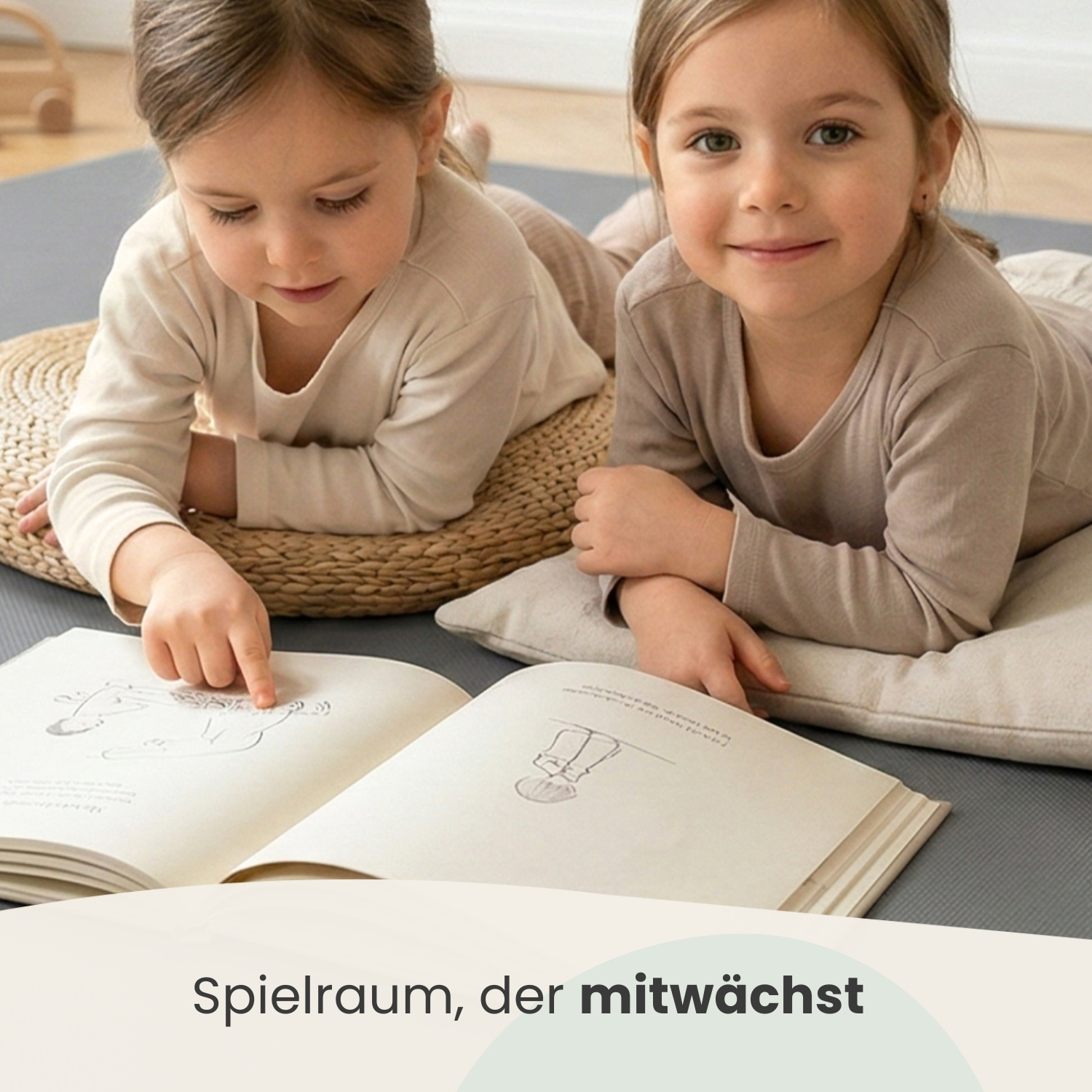 Zwei kleine Mädchen liegen auf dem Boden und schauen ein Buch an.