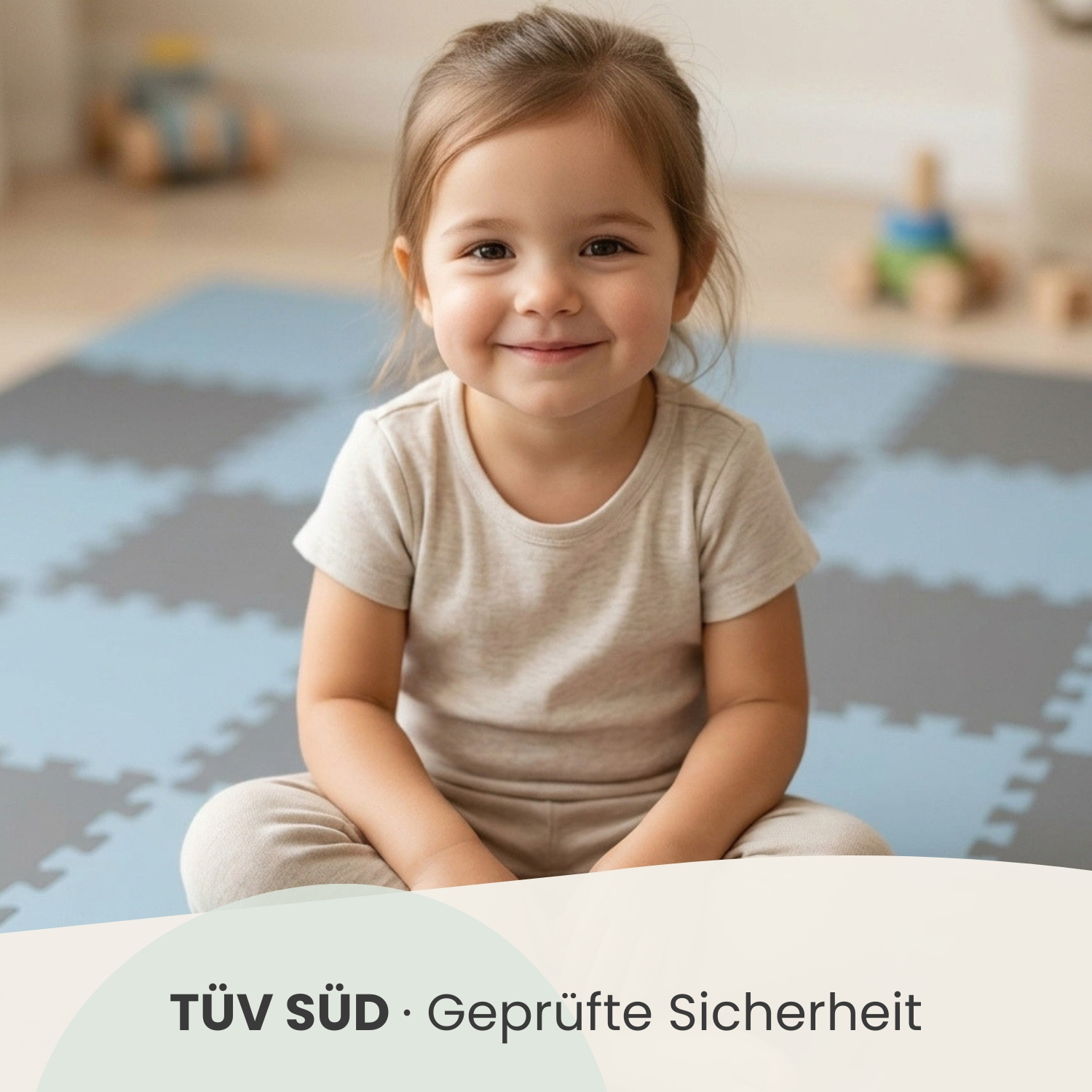Ein lächelndes kleines Mädchen sitzt auf einer blau-grauen Matte in einem Spielzimmer.
