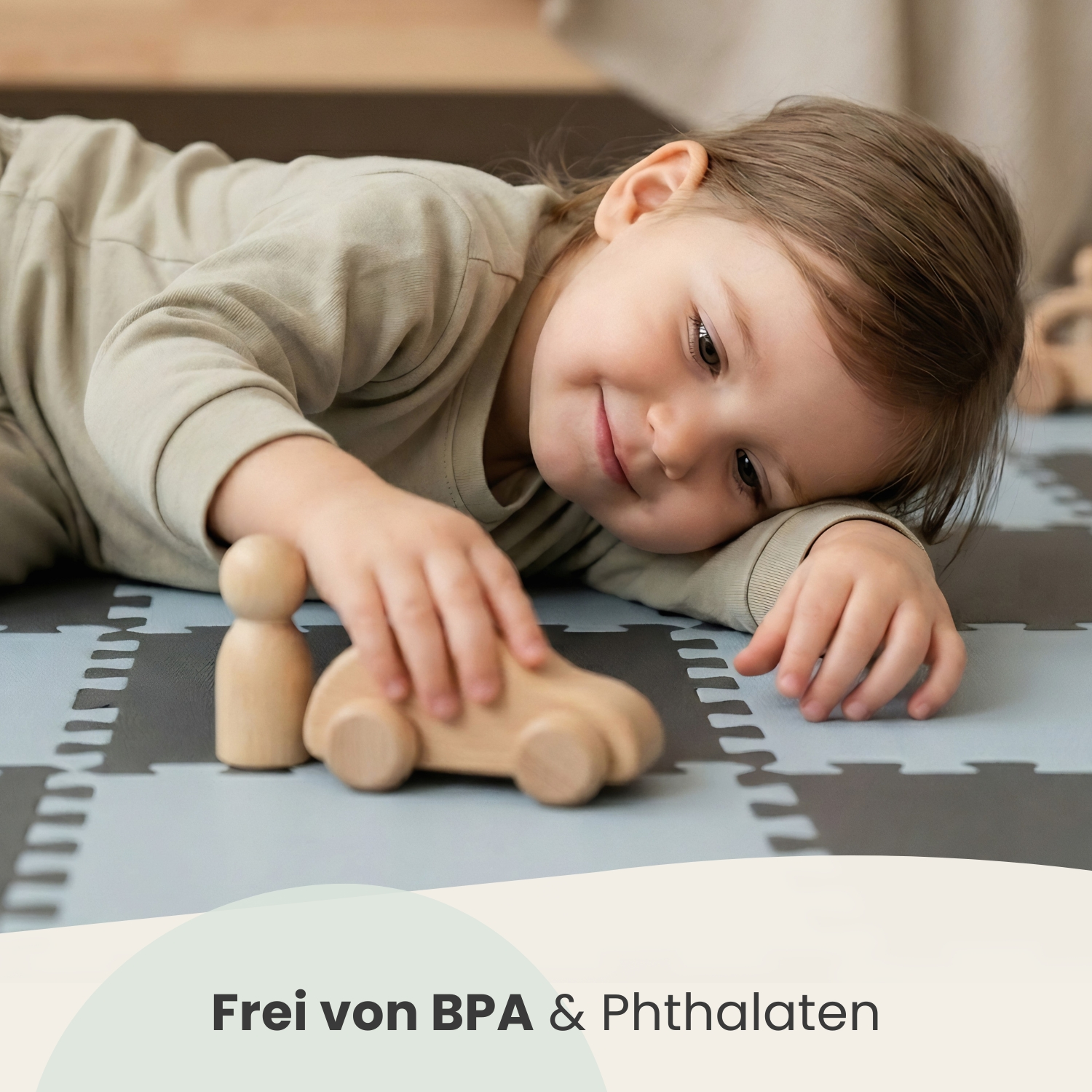 Kleines Kind liegt auf Spielmatte und spielt mit Holzauto und Figur.