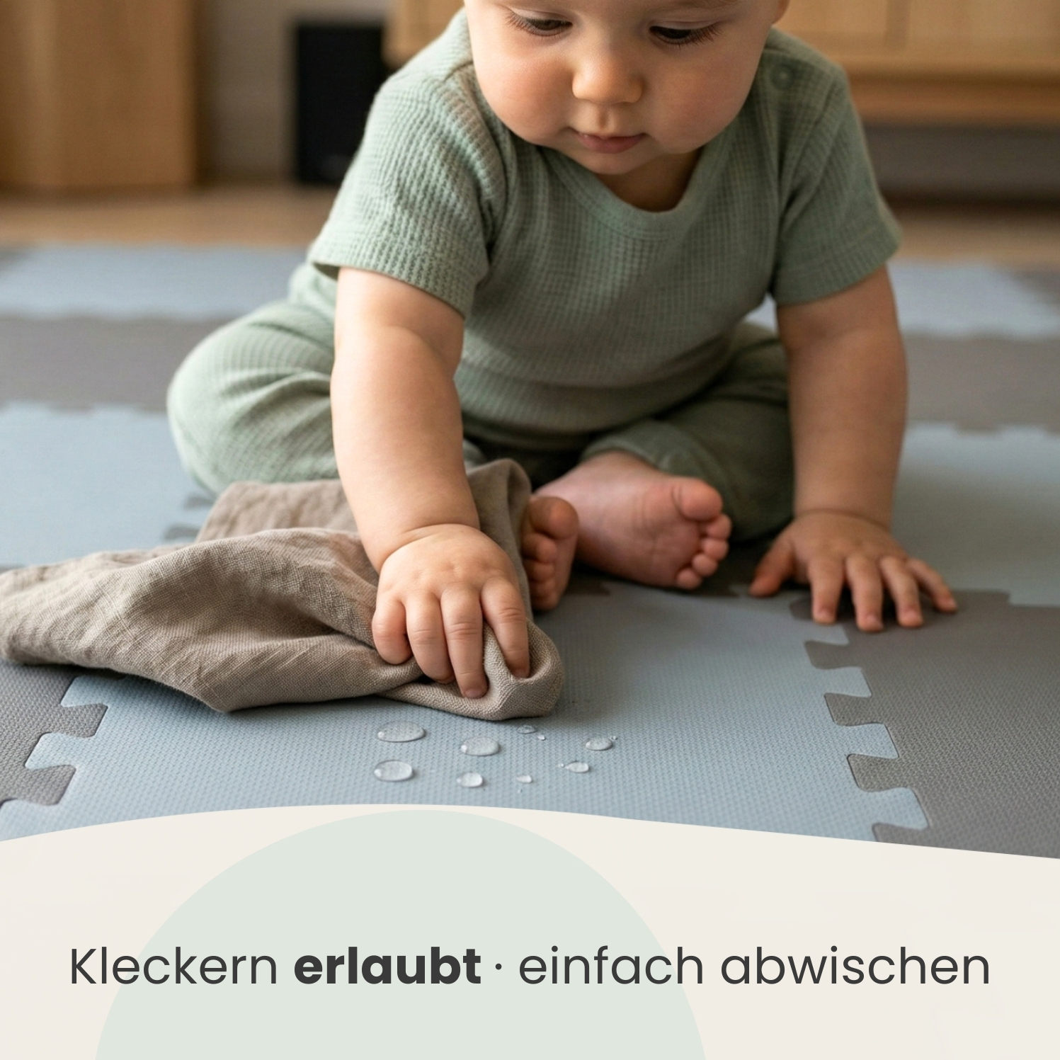 Ein Baby in einem grünen Strampler wischt mit einem Tuch über nasse Bodenteile.