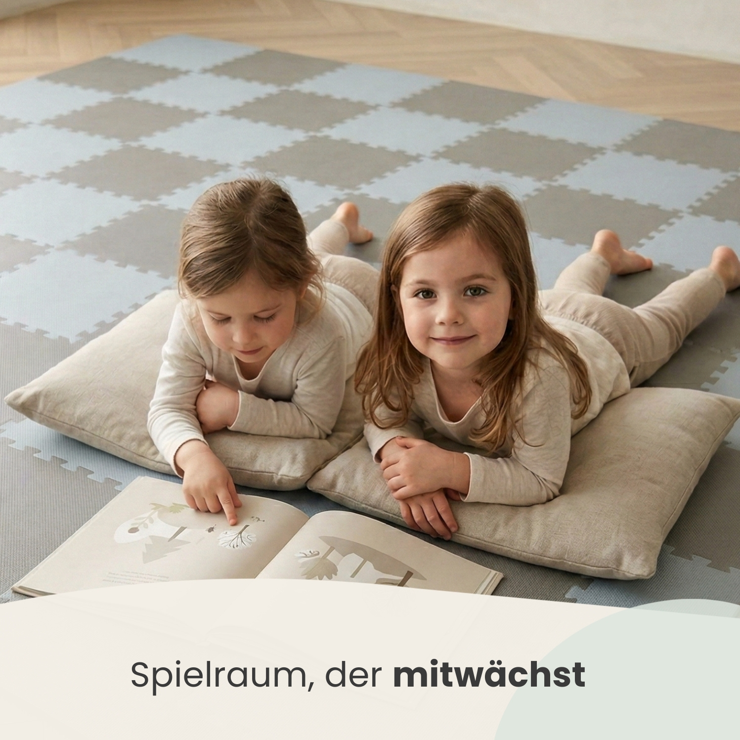 Zwei Mädchen liegen auf Kissen und lesen ein Buch auf einer Bodenmatte.