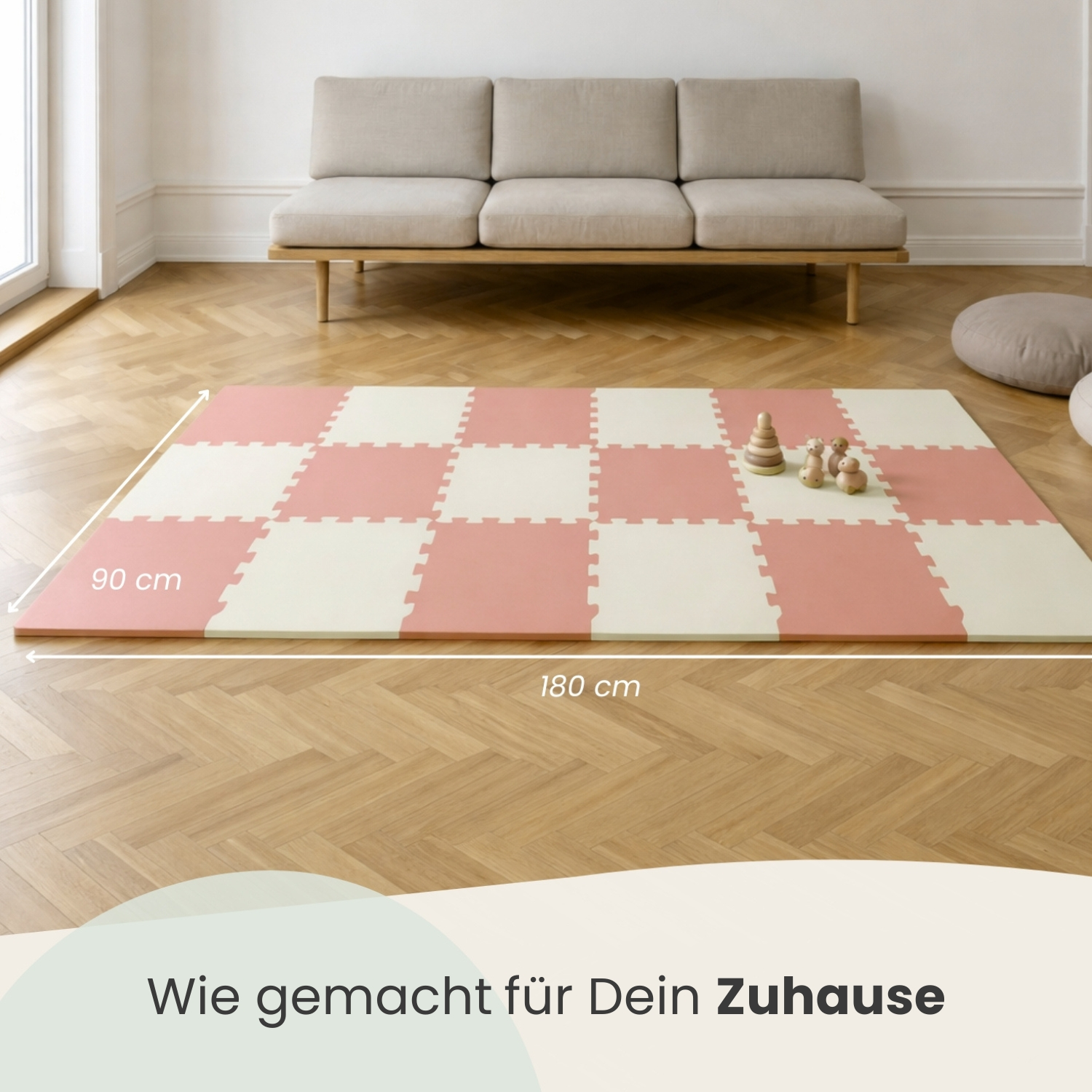 Ein Spielteppich in Rosa und Creme mit Holzspielzeug darauf, daneben ein Sofa.