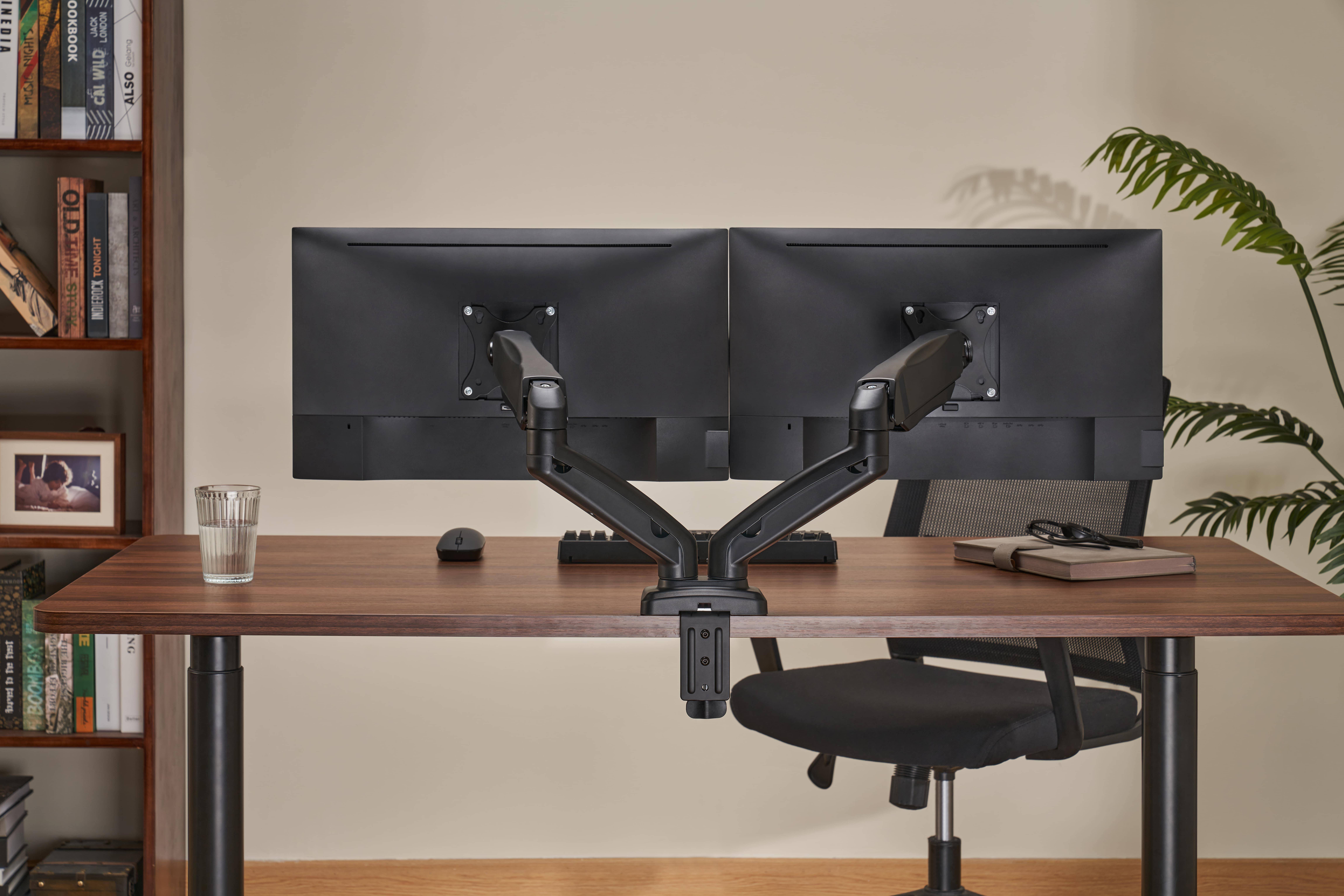 Zwei Monitore auf einem Schreibtisch mit Maus, Tastatur, Glas Wasser und Büchern.