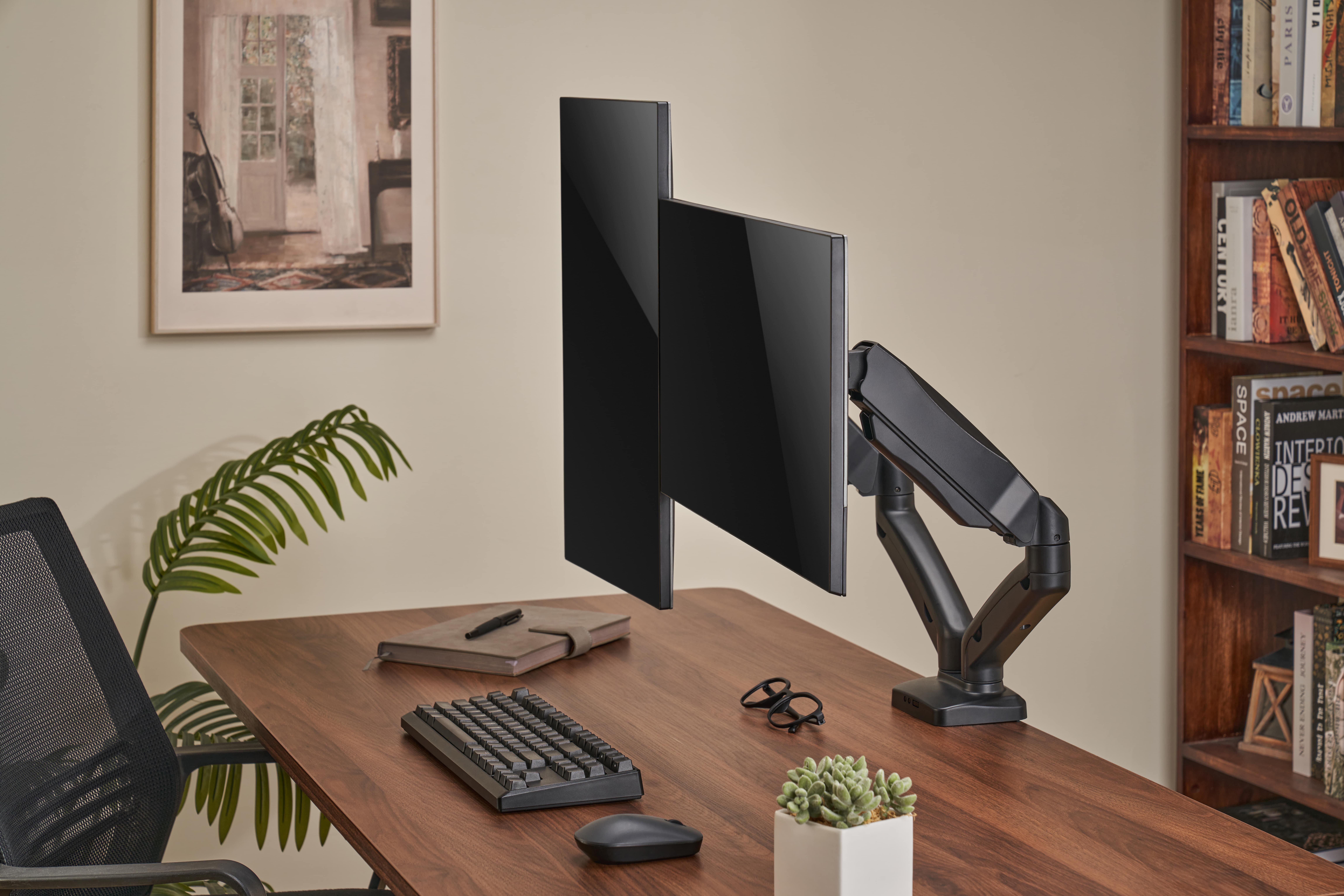 Ein Schreibtisch mit zwei Monitoren, Tastatur, Maus, Brille und Pflanze.