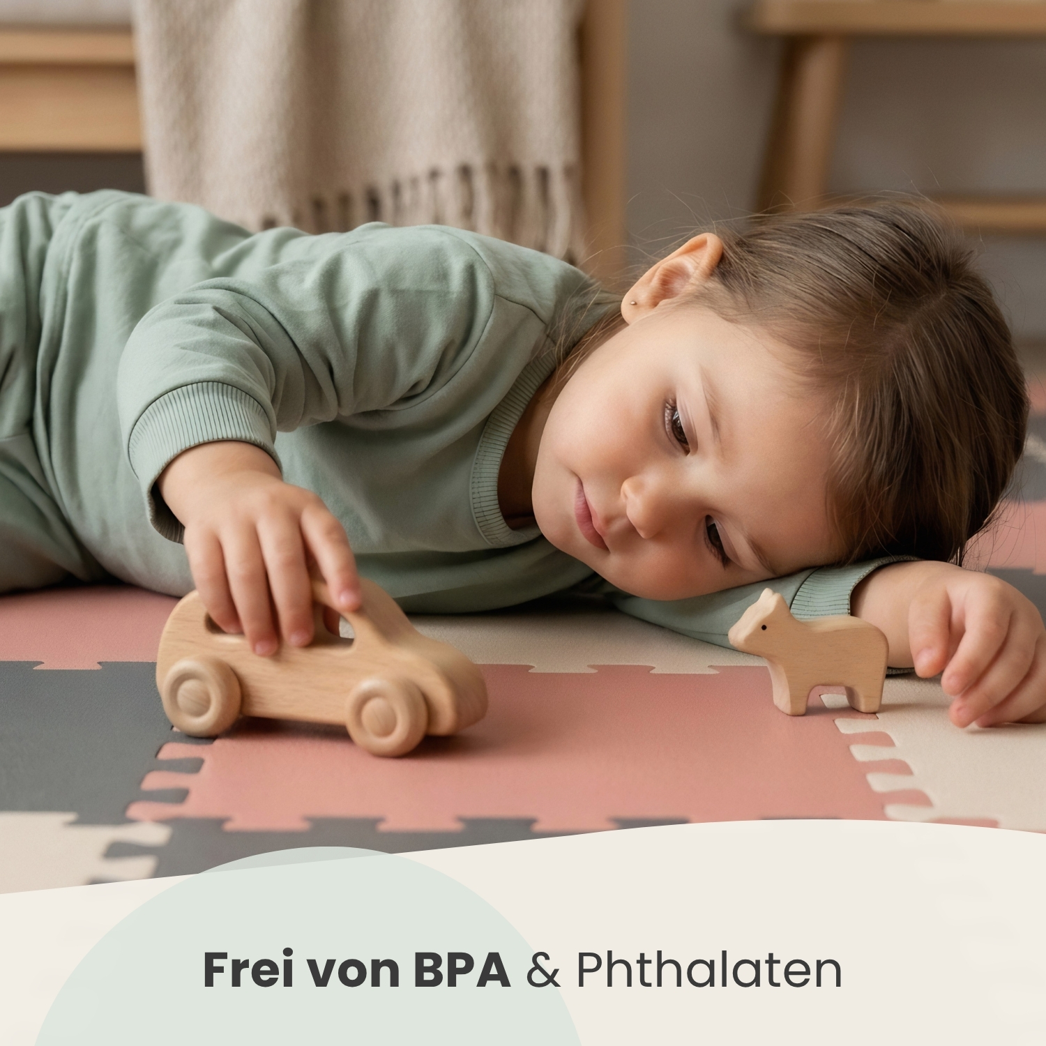 Ein kleines Kind liegt auf einer Spielmatte und spielt mit Holzspielzeugauto und -tier.