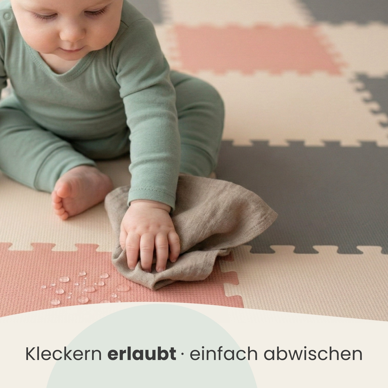 Baby wischt mit Tuch über bunte Bodenmatte, auf der Wassertropfen sind.
