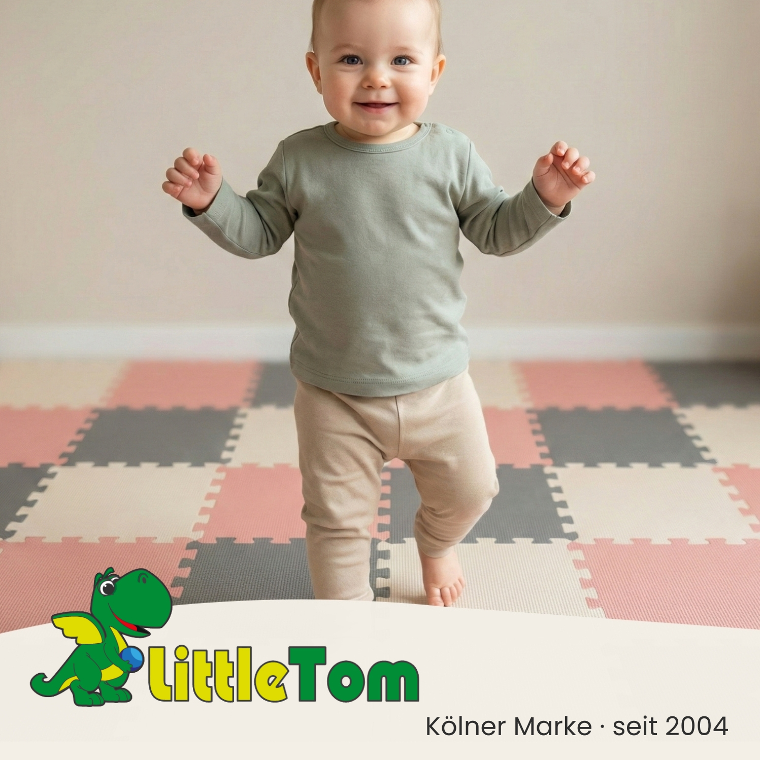 Ein lächelndes Baby in grünem Hemd und beiger Hose steht auf einer bunten Matte. Ein Cartoon-Drachenlogo ist sichtbar.
