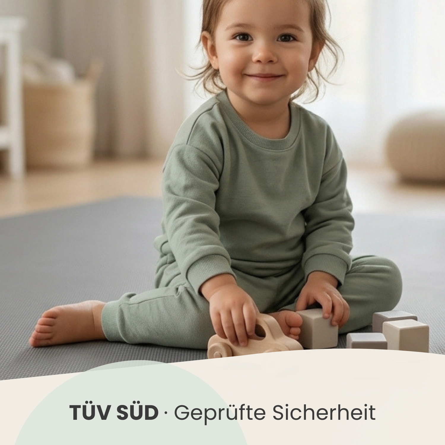 Ein Kleinkind in einem grünen Outfit spielt mit Holzspielzeug auf einer grauen Matte.