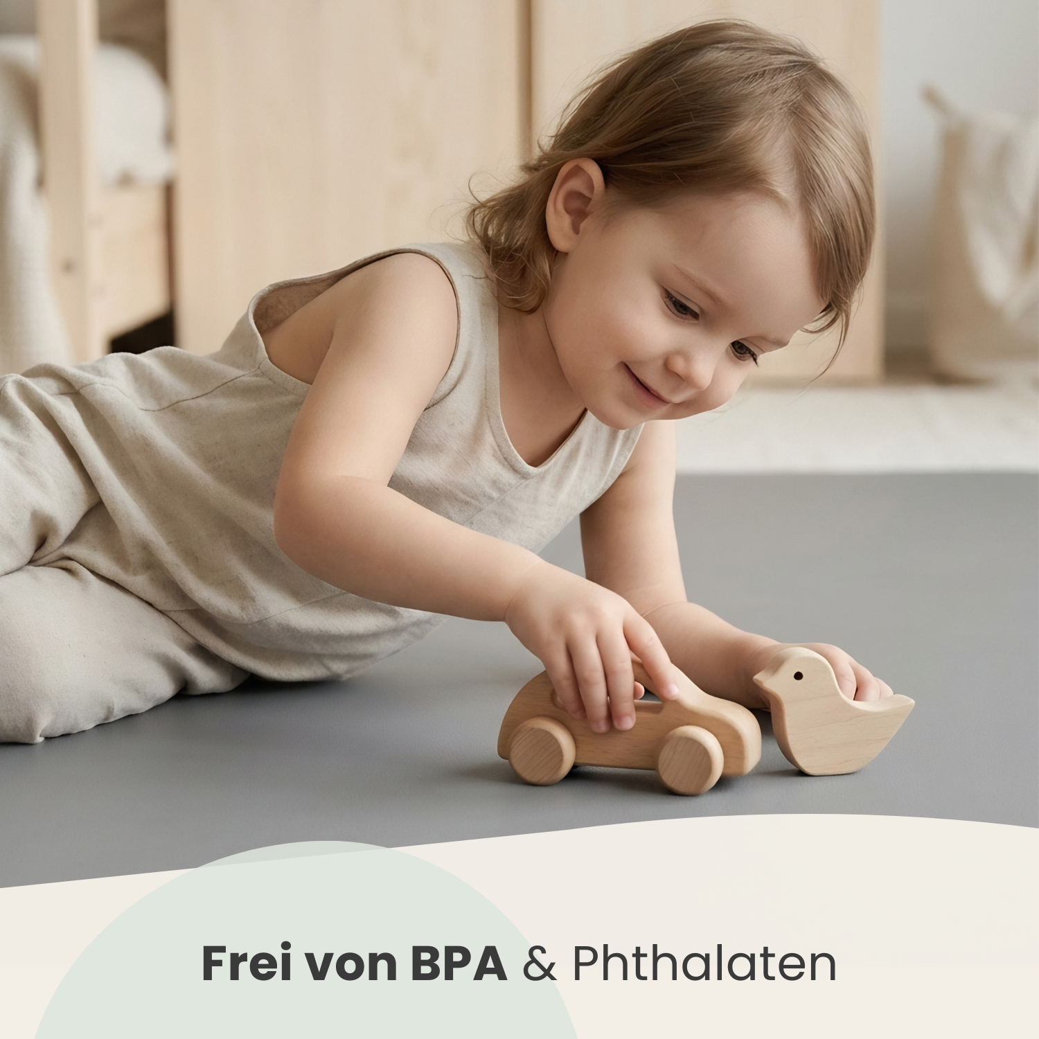 Ein kleines Kind spielt mit Holzspielzeugauto und Vogel auf grauem Teppich.