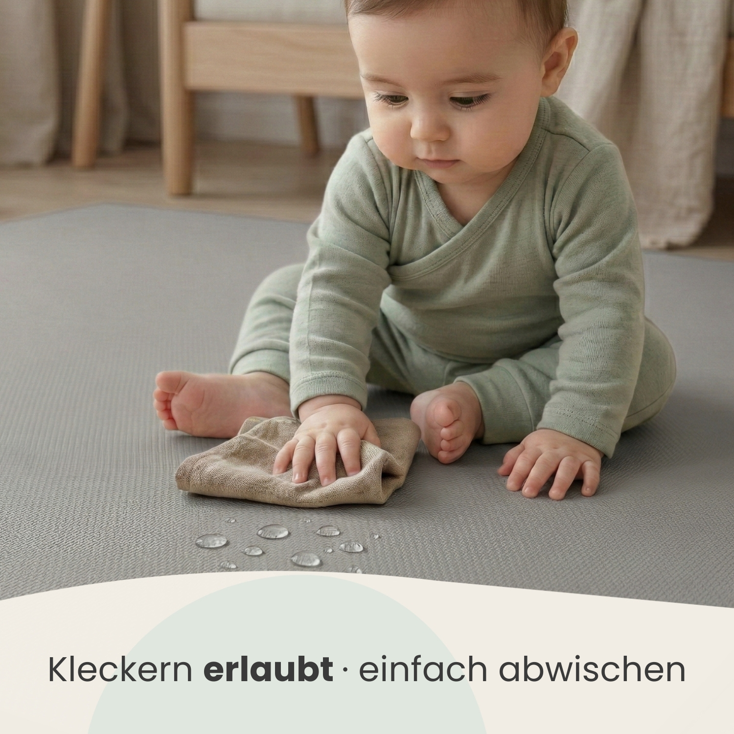Baby wischt mit einem Tuch über eine Matte, auf der Wassertropfen sind.