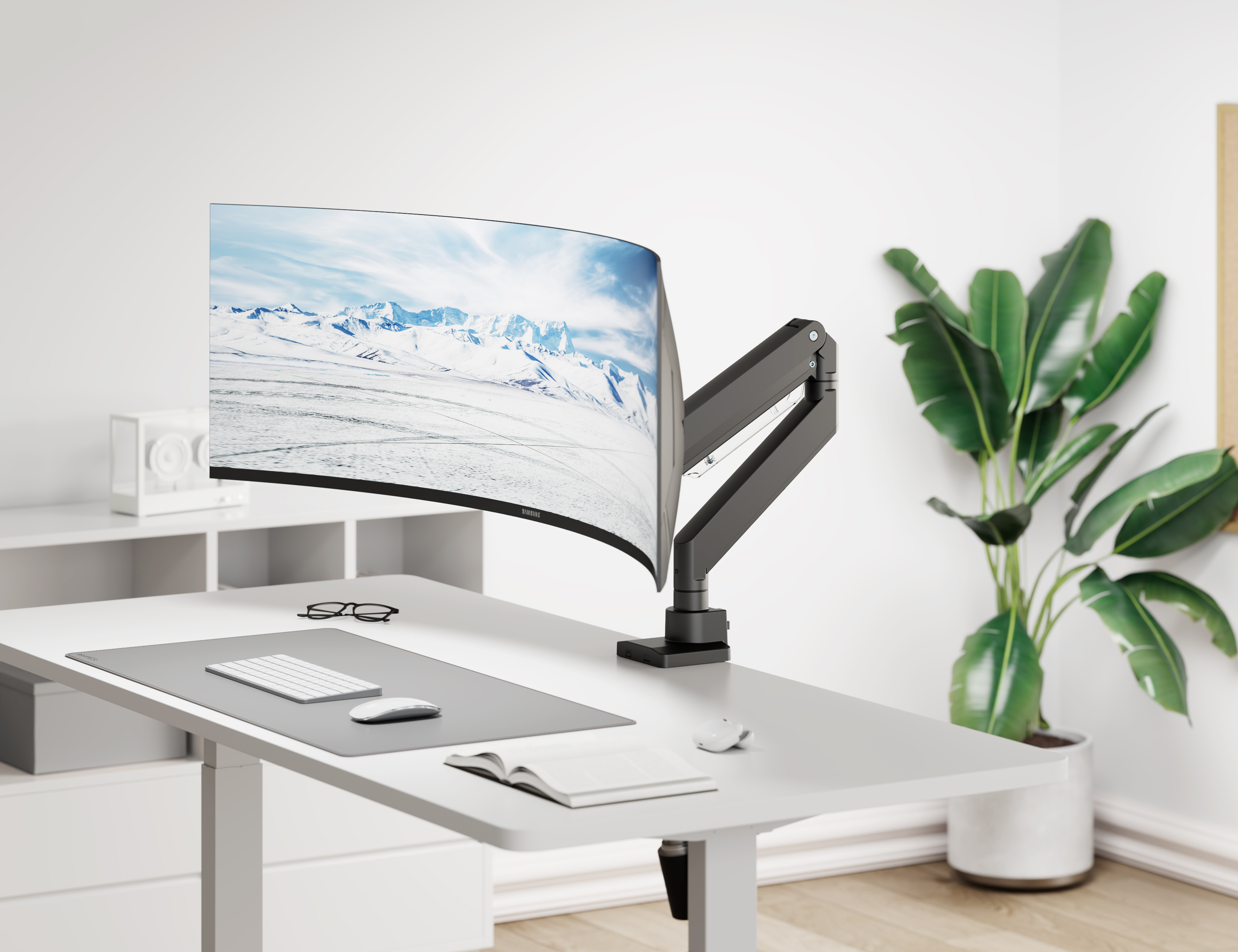 Ein gebogener Monitor mit Berglandschaft auf einem Schreibtisch, daneben eine Pflanze.