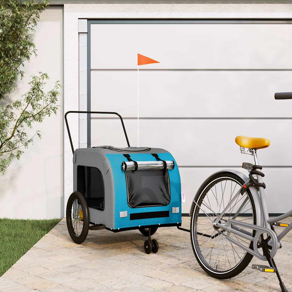 Ein blauer und grauer Hundanhänger mit orangem Wimpel neben einem Fahrrad vor einer Garage.
