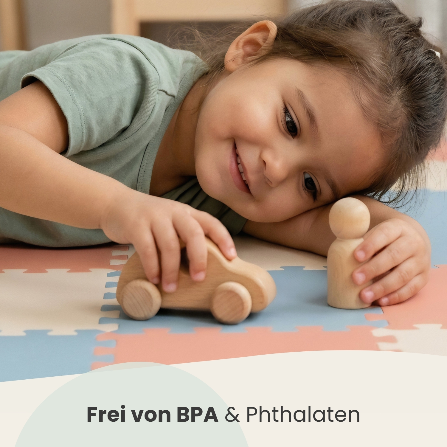 Kleines Mädchen spielt mit Holzauto und Holzfigur auf bunter Matte.