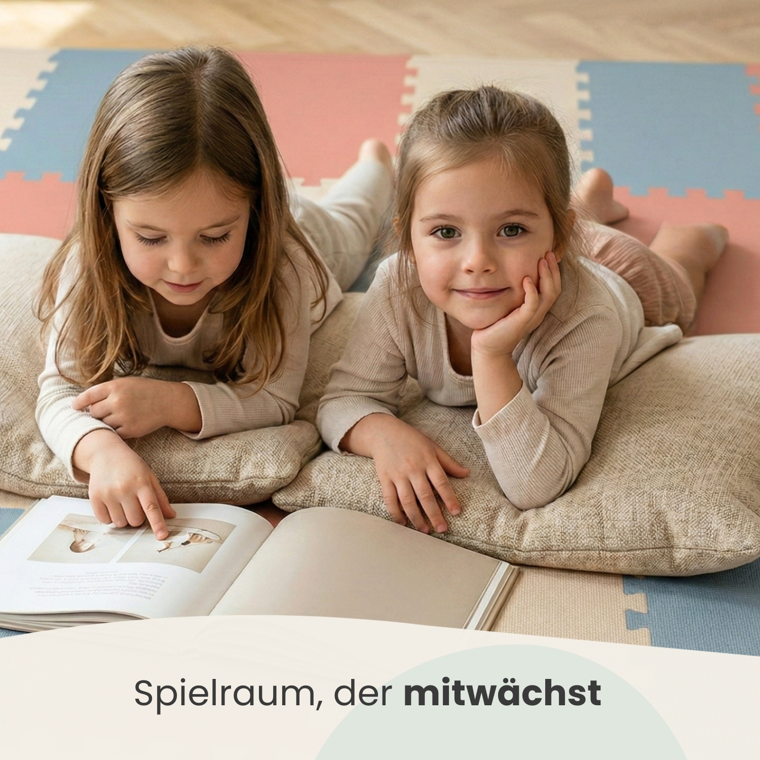 Zwei Mädchen liegen auf Kissen und lesen ein Buch. Sie liegen auf einer bunten Matte.