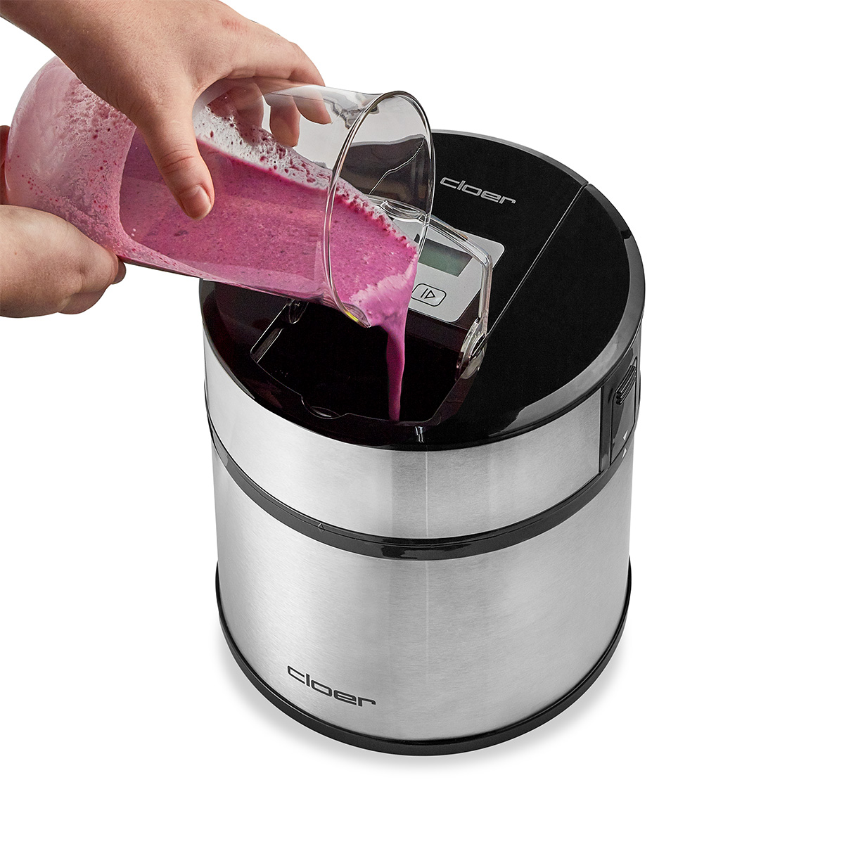 Eine Hand gießt pinken Smoothie aus einem Glaskrug in ein silbernes und schwarzes Gerät.